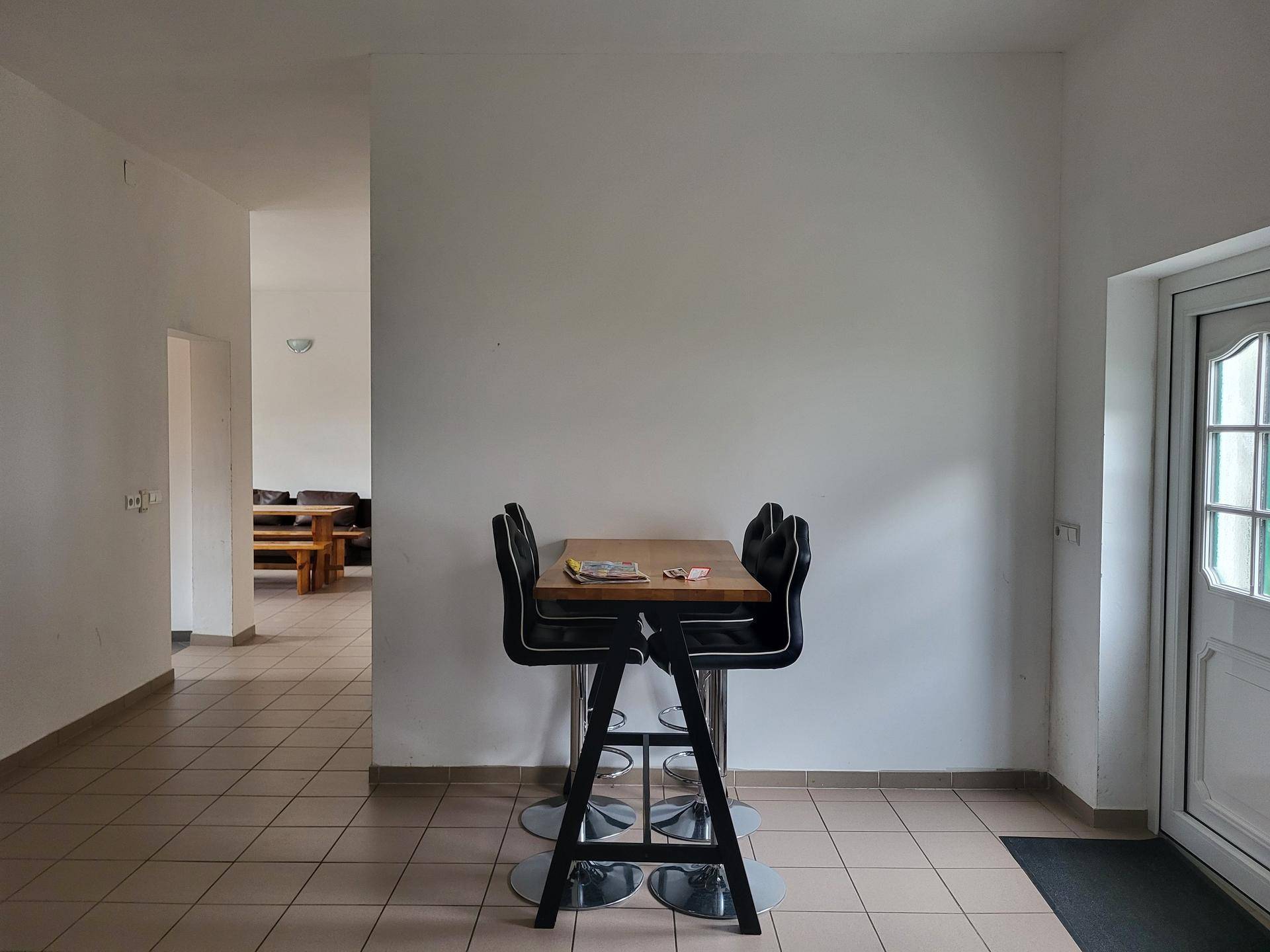 Heller Essbereich mit Bartisch und Hockern, Fliesenboden und Zugang zu einem weiteren Raum.