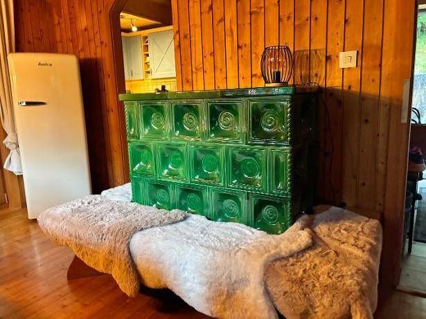Ein traditioneller grüner Kachelofen als Heizelement in einem Raum mit Holzwänden und einem Kühlschrank.