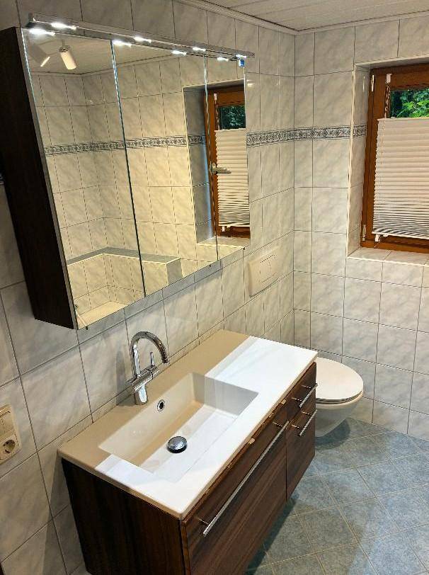 Gefliestes Badezimmer mit modernem Waschtisch, Spiegelschrank und wandhängendem WC.