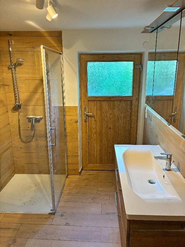 Modernes Badezimmer mit ebenerdiger Dusche und Waschtisch, ausgestattet mit Holzoptik-Fliesen.