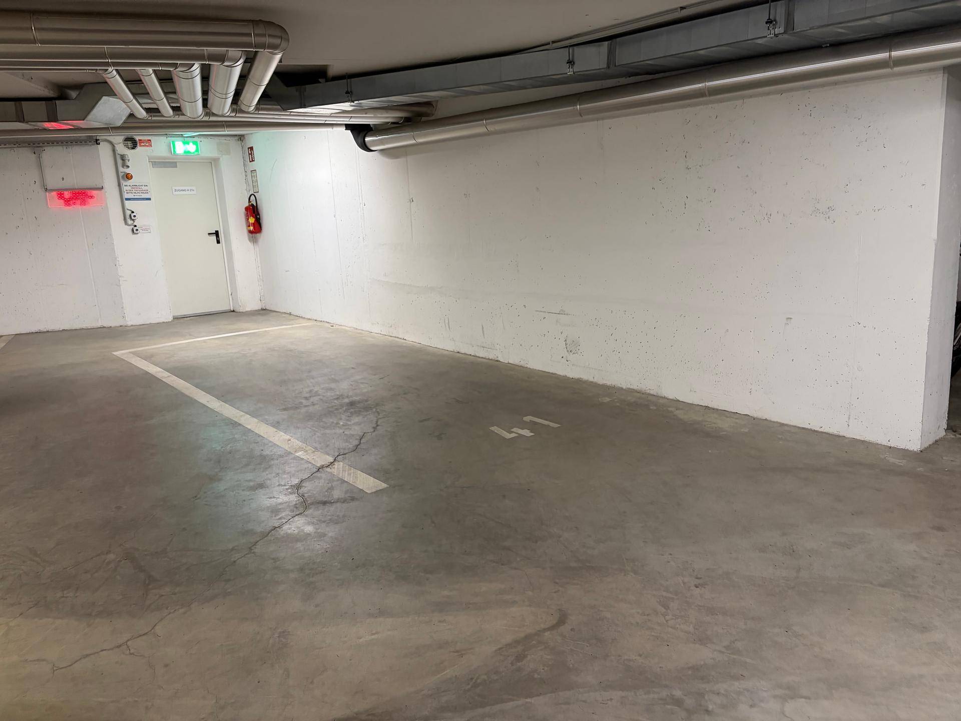 Tiefgaragenstellplatz Nummer 41 mit robustem Betonboden, umgeben von weißen Wänden und Deckeninstallationen, bereit zur Nutzung.