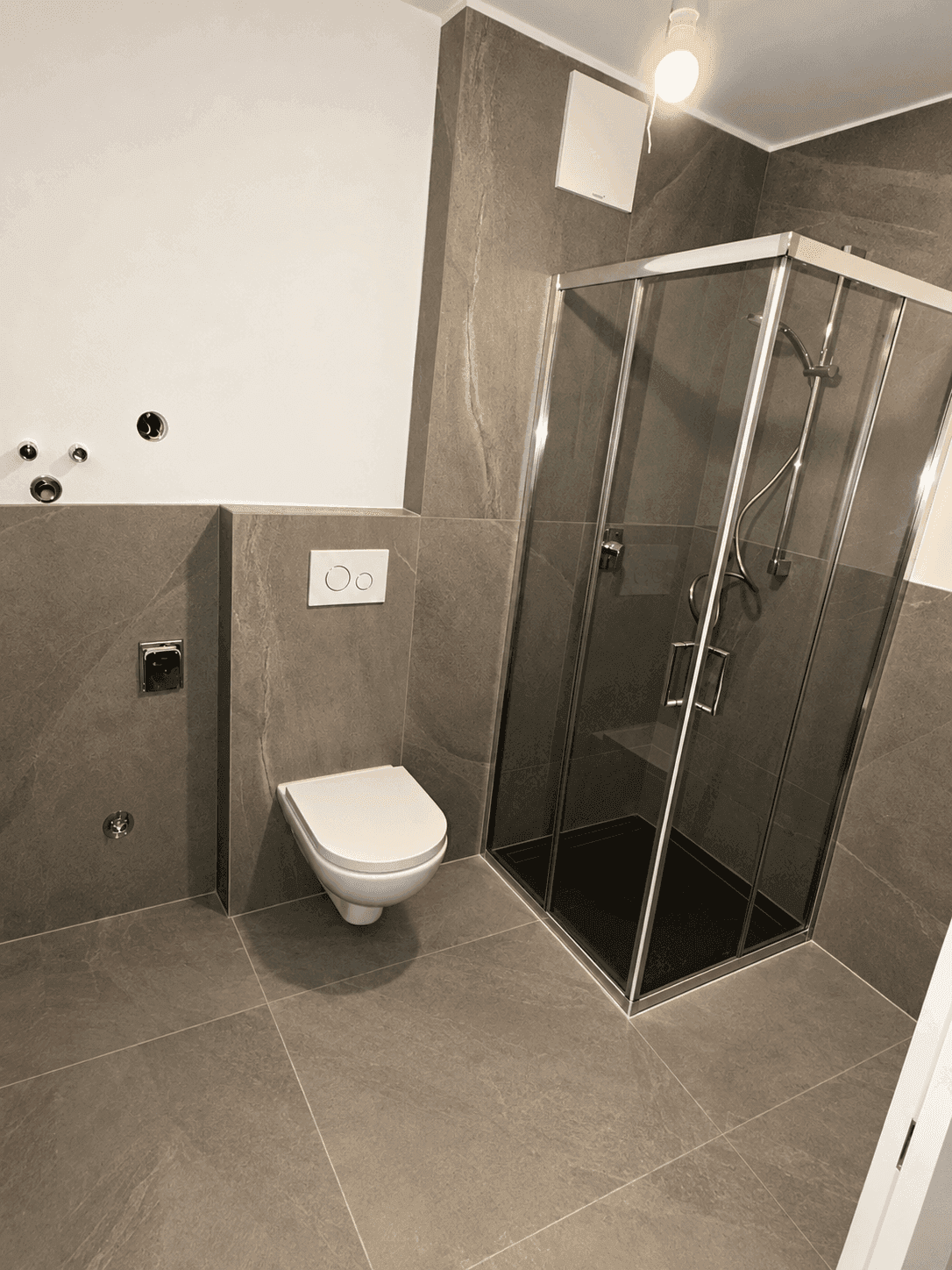 Modernes Badezimmer mit grauen Großformatfliesen, Duschkabine und wandhängendem WC.