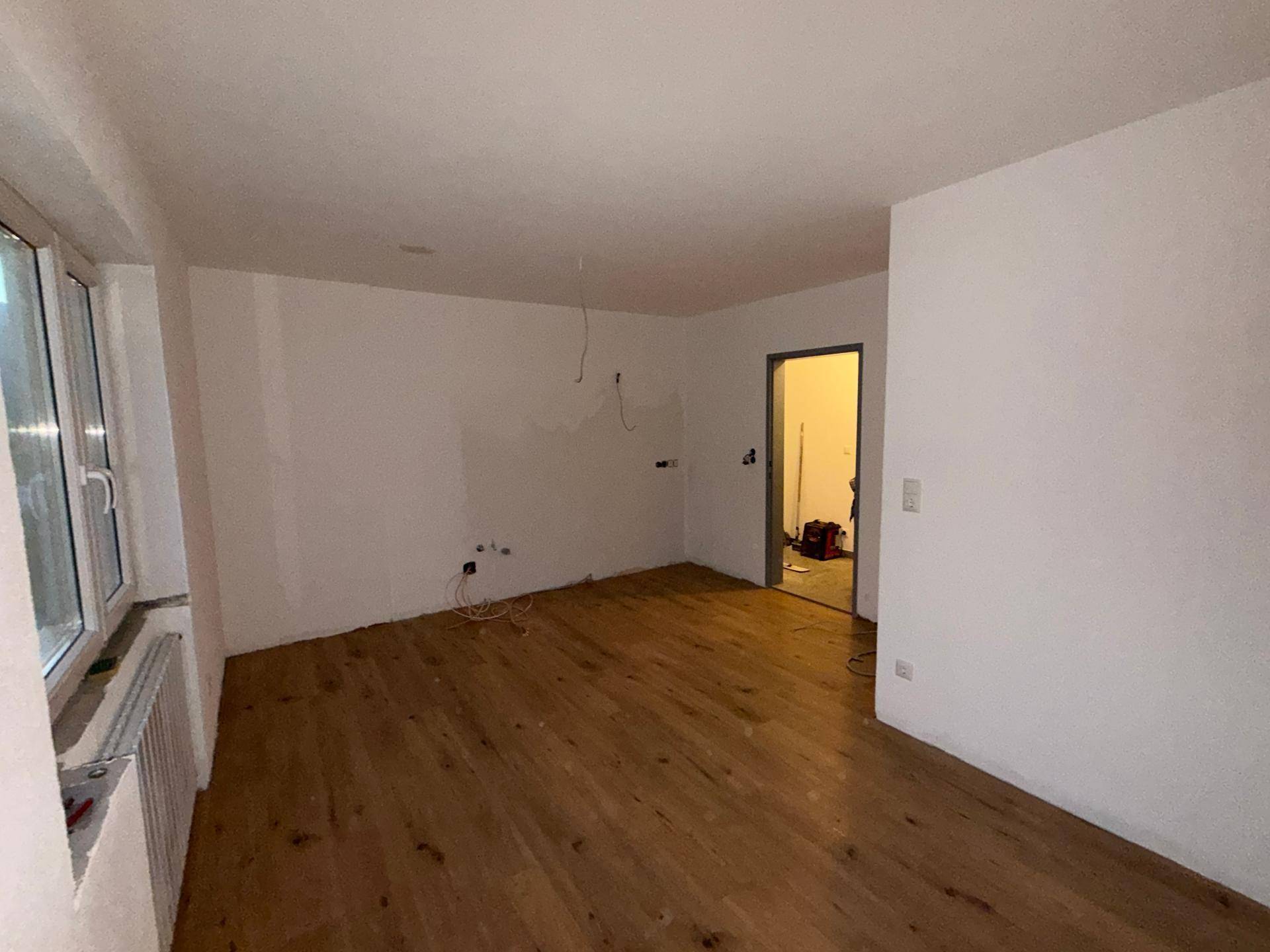 Geräumiges, unmöbliertes Zimmer mit Holzboden und Fenster, ideal als Wohnbereich.