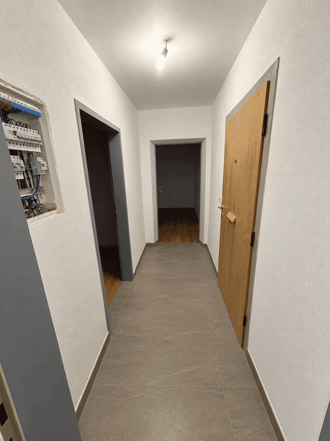 Heller Flur mit modernen grauen Fliesen und Holztüren, der zu weiteren Räumen führt.