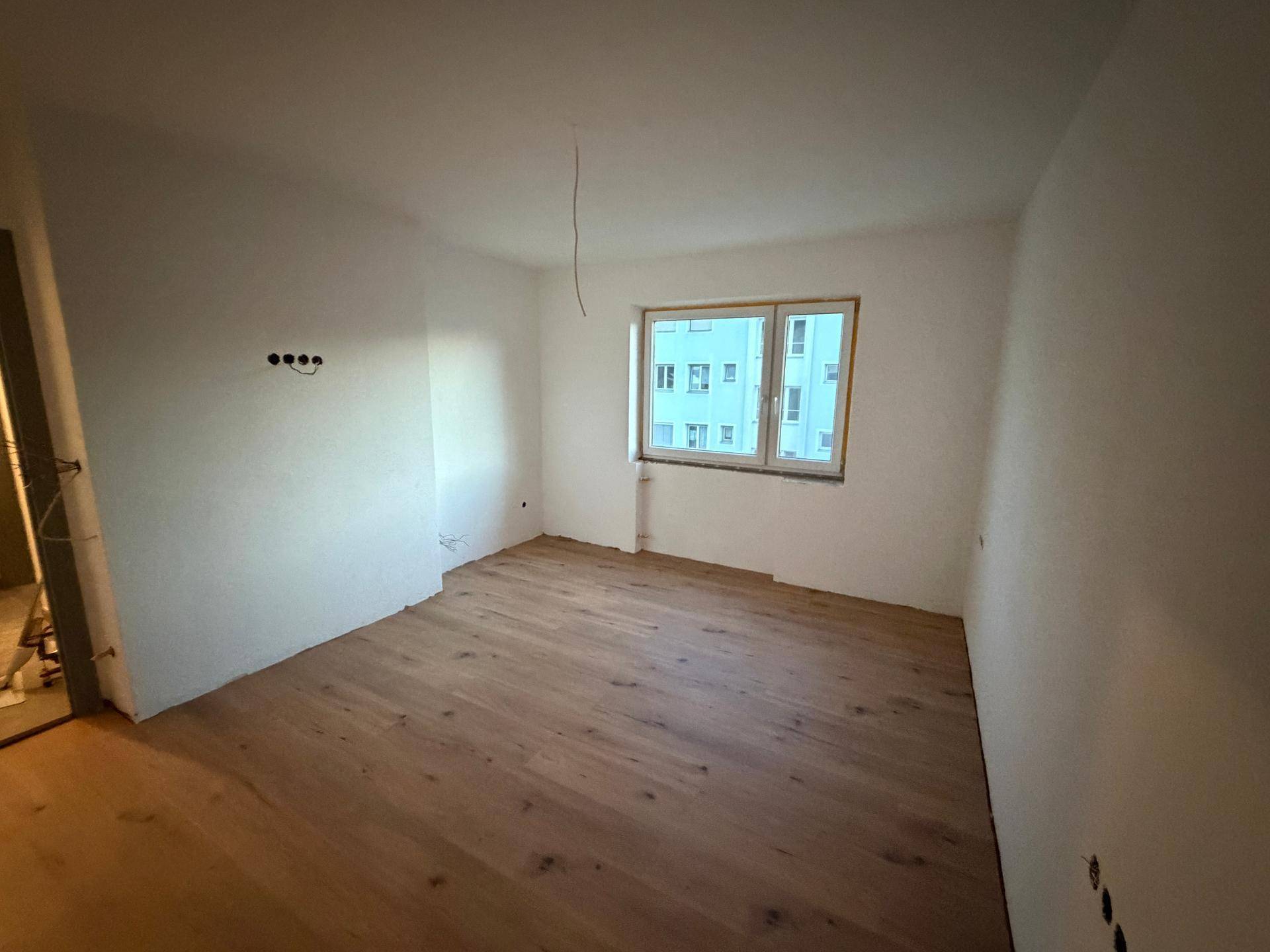Leeres Zimmer mit hellem Holzboden und Fenster, bereit für die individuelle Gestaltung.