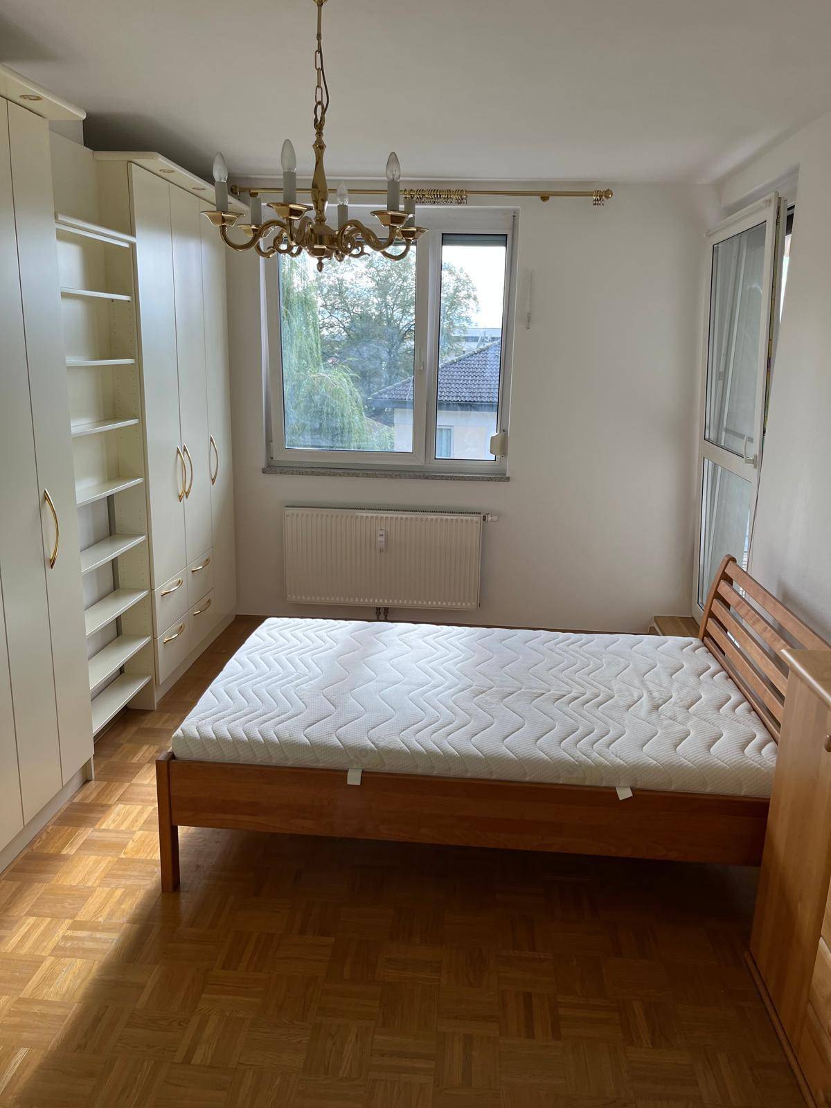 Schlafzimmer mit Holzbett, geräumigen Einbauschränken, Parkettboden und großem Fenster.