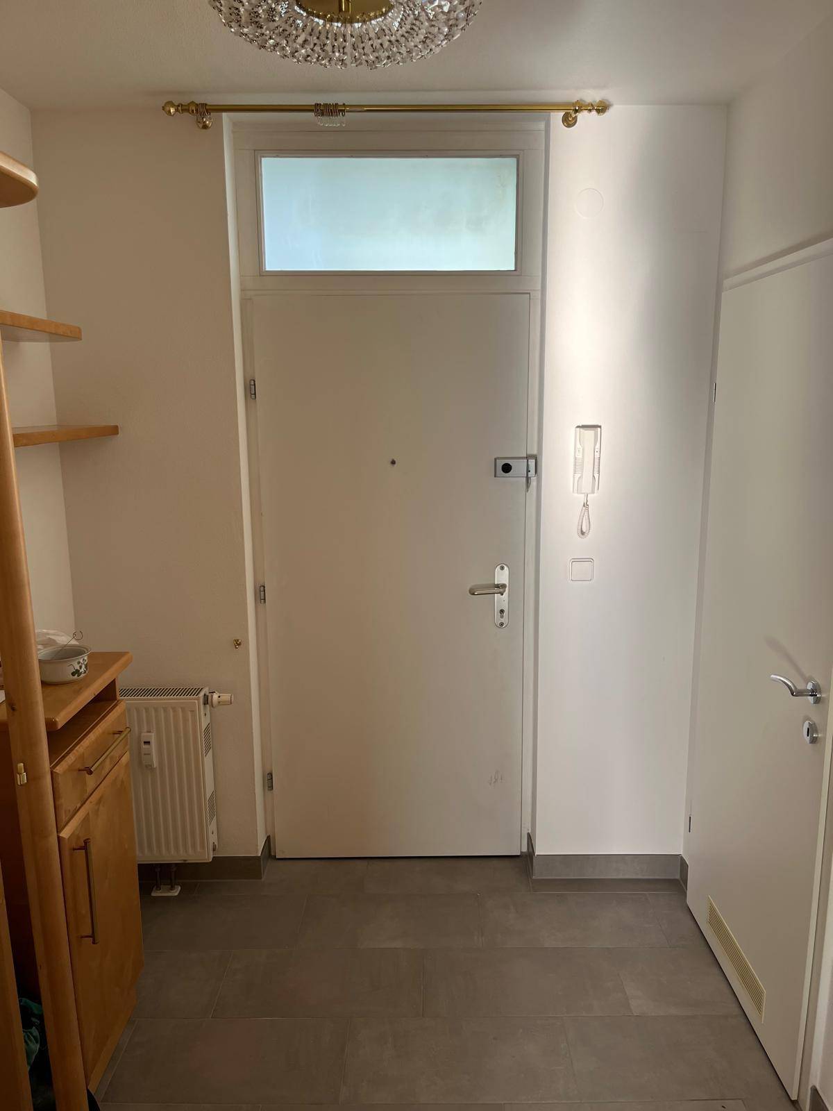 Eingangsbereich mit Haustür, Fliesenboden und einfacher Garderobe.