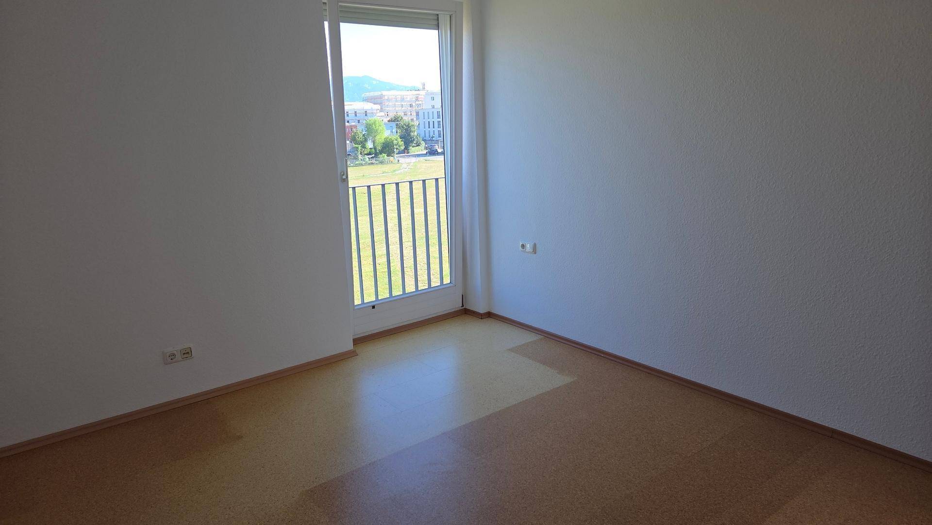 Schlafzimmer mit Laminatboden und Fenster mit Blick ins Grüne und auf die Umgebung.