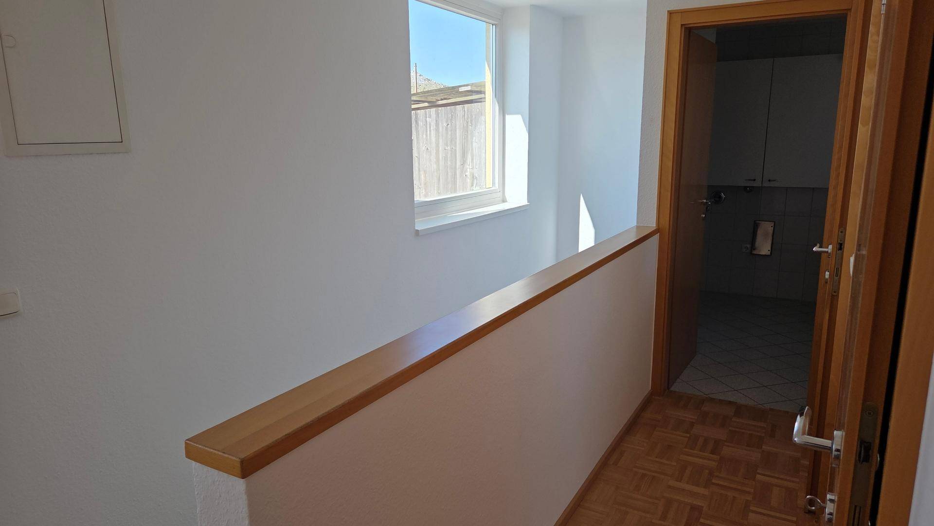 Heller Flur im Obergeschoss mit Holzgeländer und Fenster, bietet Zugang zu weiteren Räumen.
