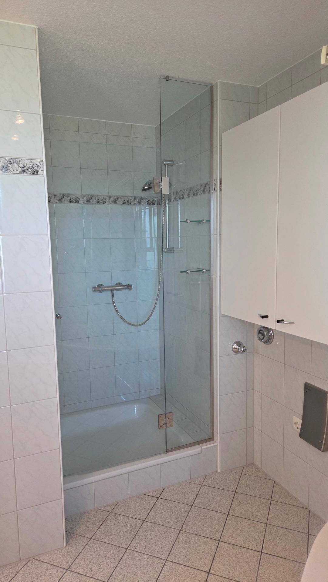 Badezimmer mit Duschkabine, Fliesenboden und weißen Wandschränken.