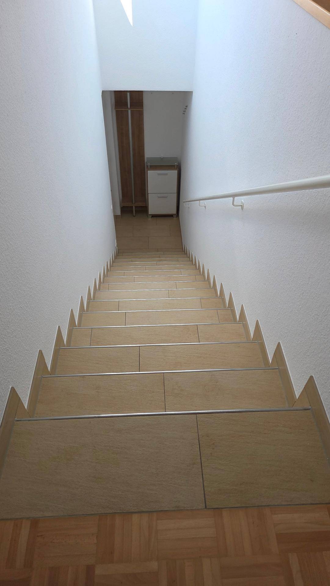 Treppenhaus mit Holzstufen und weiß gestrichenen Wänden, führt in den unteren Bereich.
