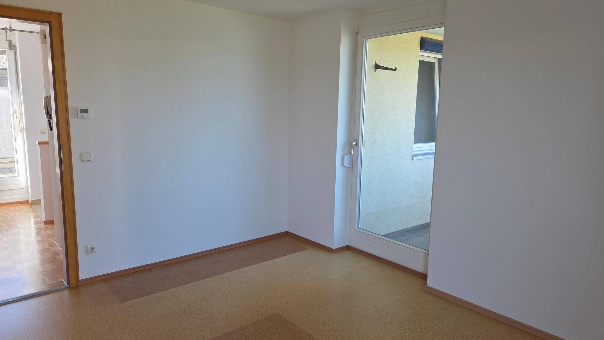 Helles Zimmer mit Zugang zu einem kleinen Balkon, ausgestattet mit Laminatboden.