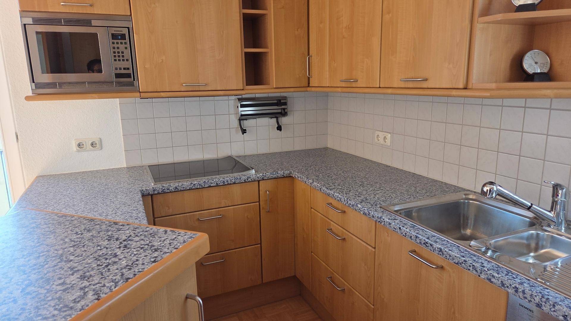 Funktionale Küche mit Holzschränken, Granit-Arbeitsplatten und integrierten Geräten.