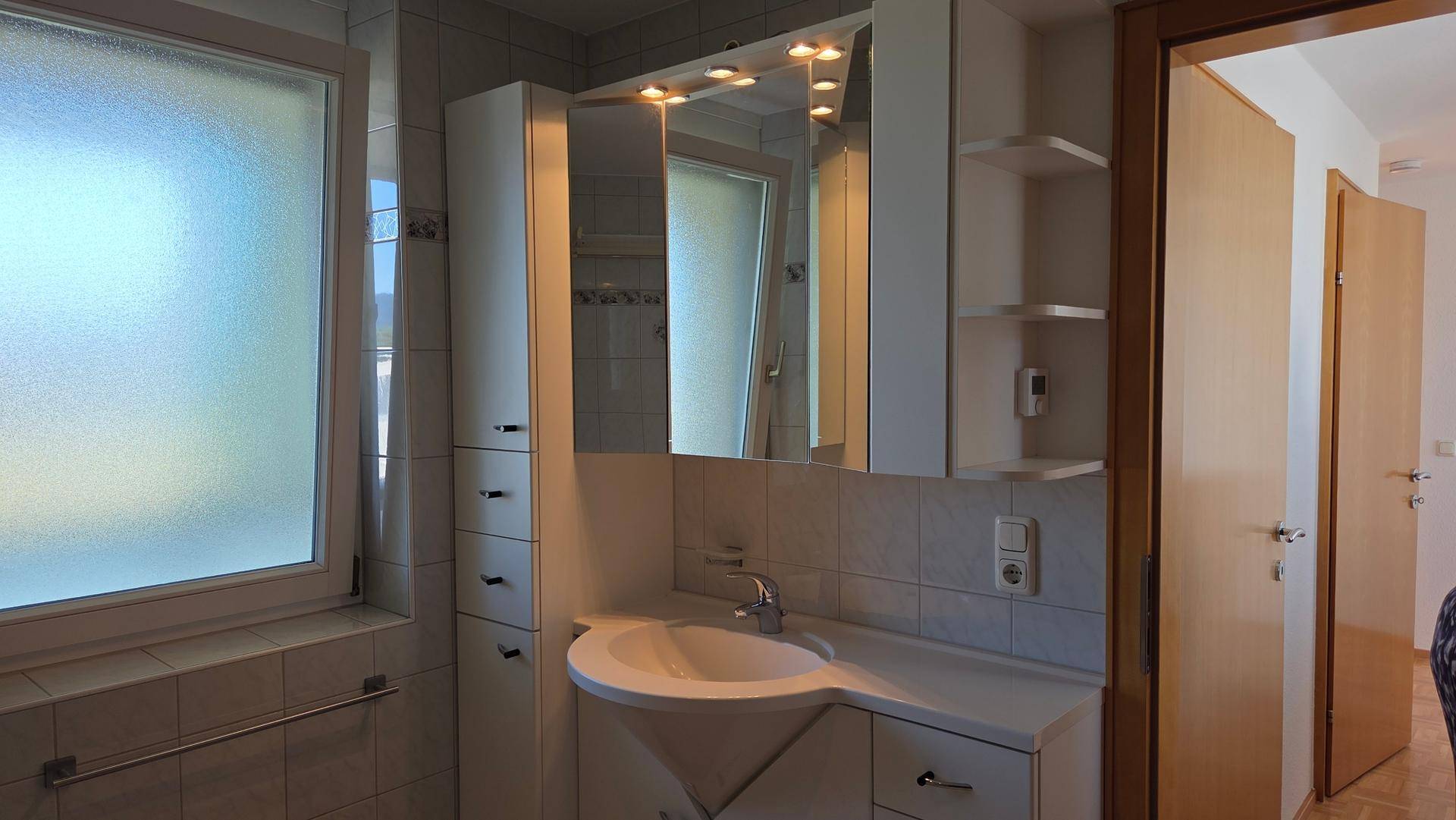 Badezimmer mit Waschbecken, Spiegelschrank und Fenster für Tageslicht.