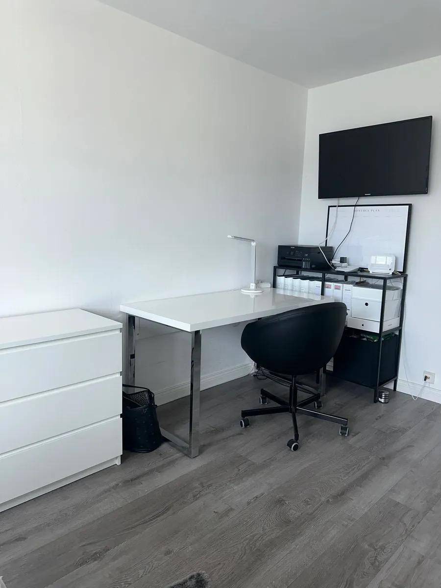Moderner Arbeitsplatz mit Schreibtisch, Bürostuhl und Wandfernseher in einem hellen Raum.