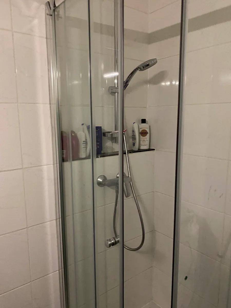 Duschkabine mit Glaswänden und Duscharmatur in einem gefliesten Badezimmer.