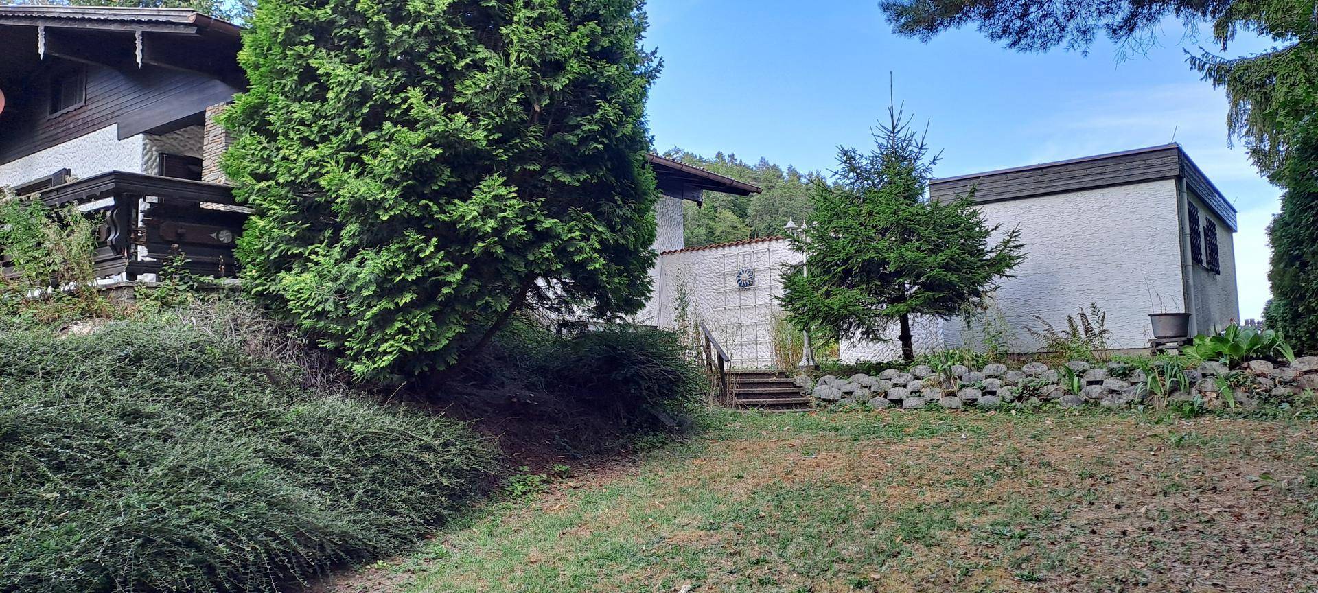 Panoramablick auf das Anwesen mit Haus, Nebengebäude, Steinmauer und Rasenfläche.