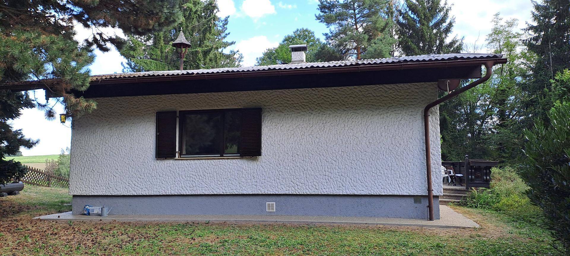 Seitenansicht des Hauses mit weißer Fassade, dunklem Dach und einem Fenster mit Fensterläden.