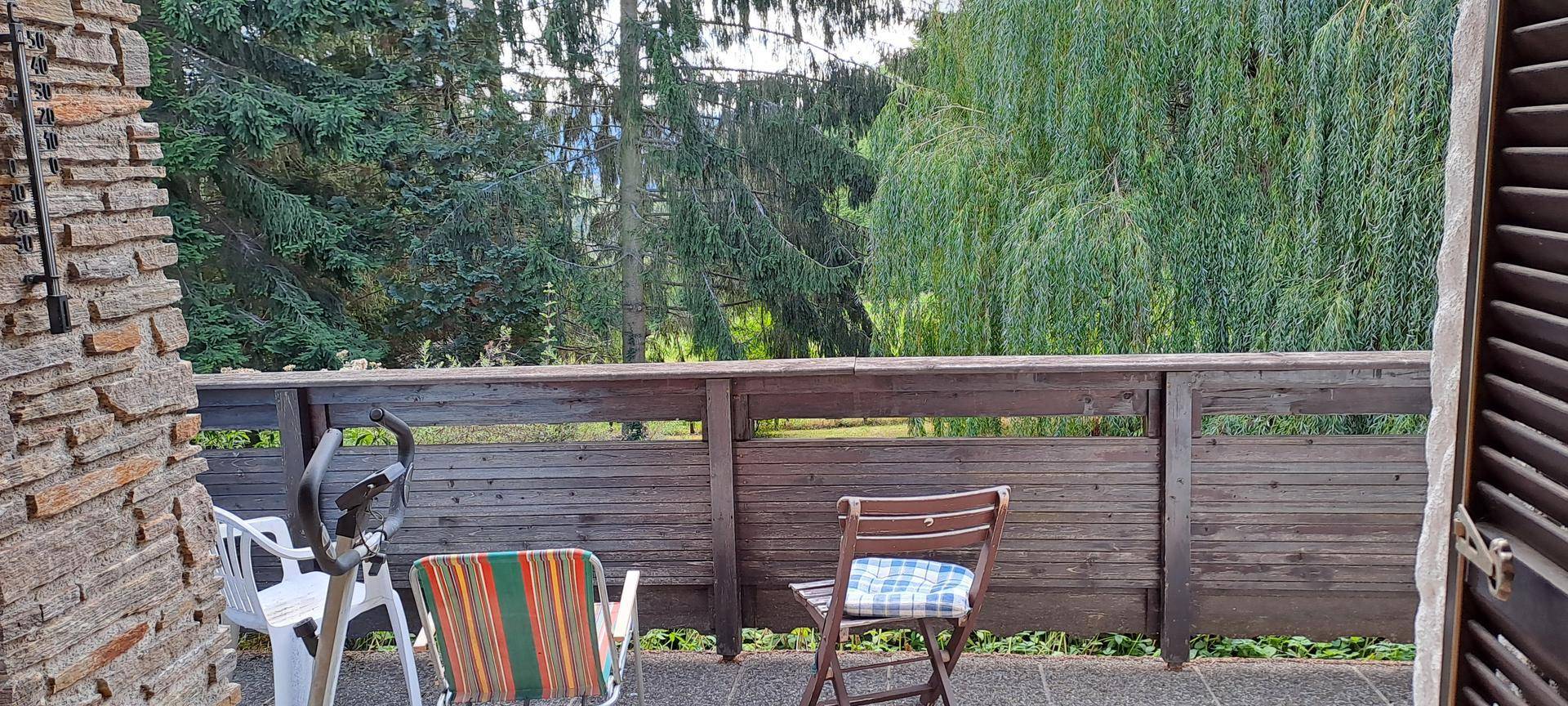 Balkon mit Holzgeländer, Gartenmöbeln und einem schönen Blick auf grüne Bäume.