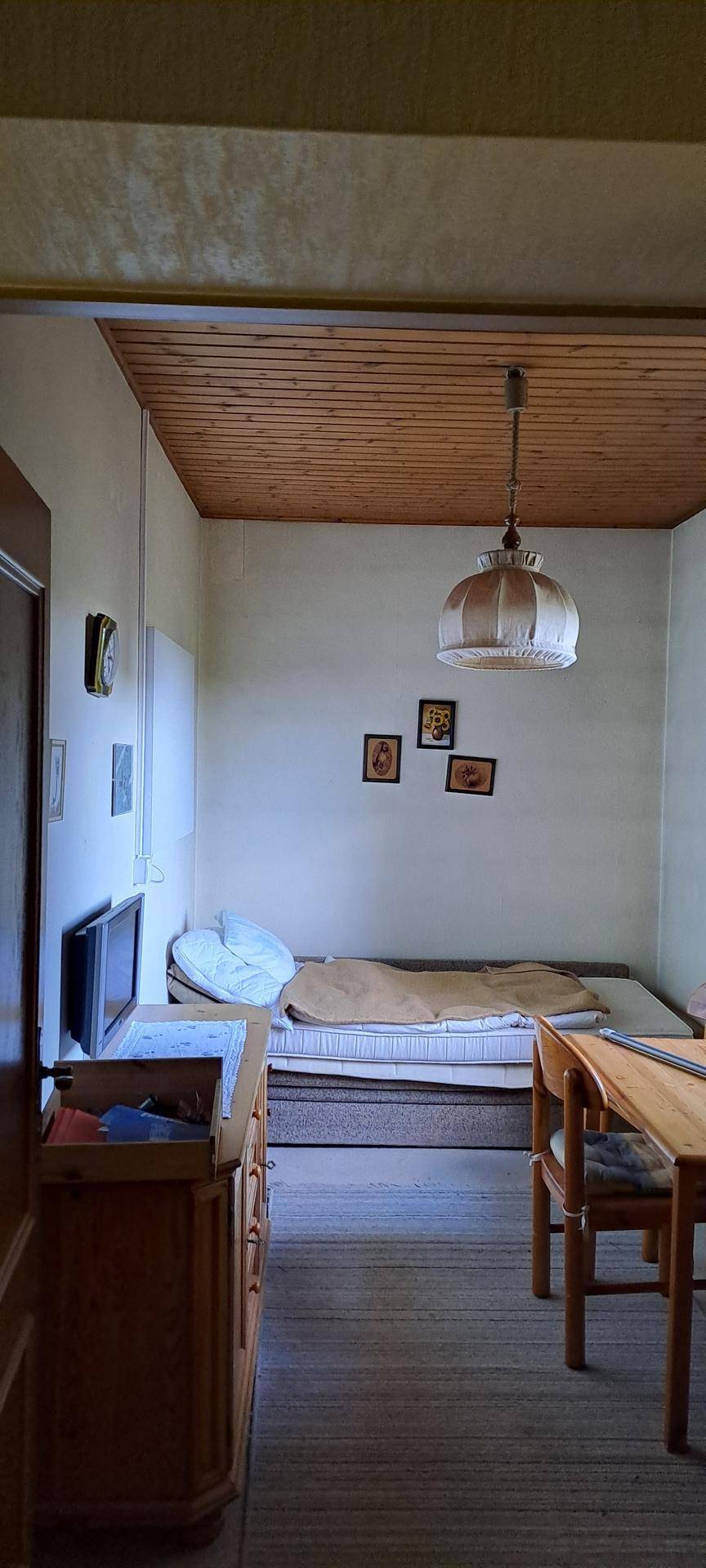 Einfaches Schlafzimmer mit Holzbalkendecke, Einzelbett und schlichten Möbeln.