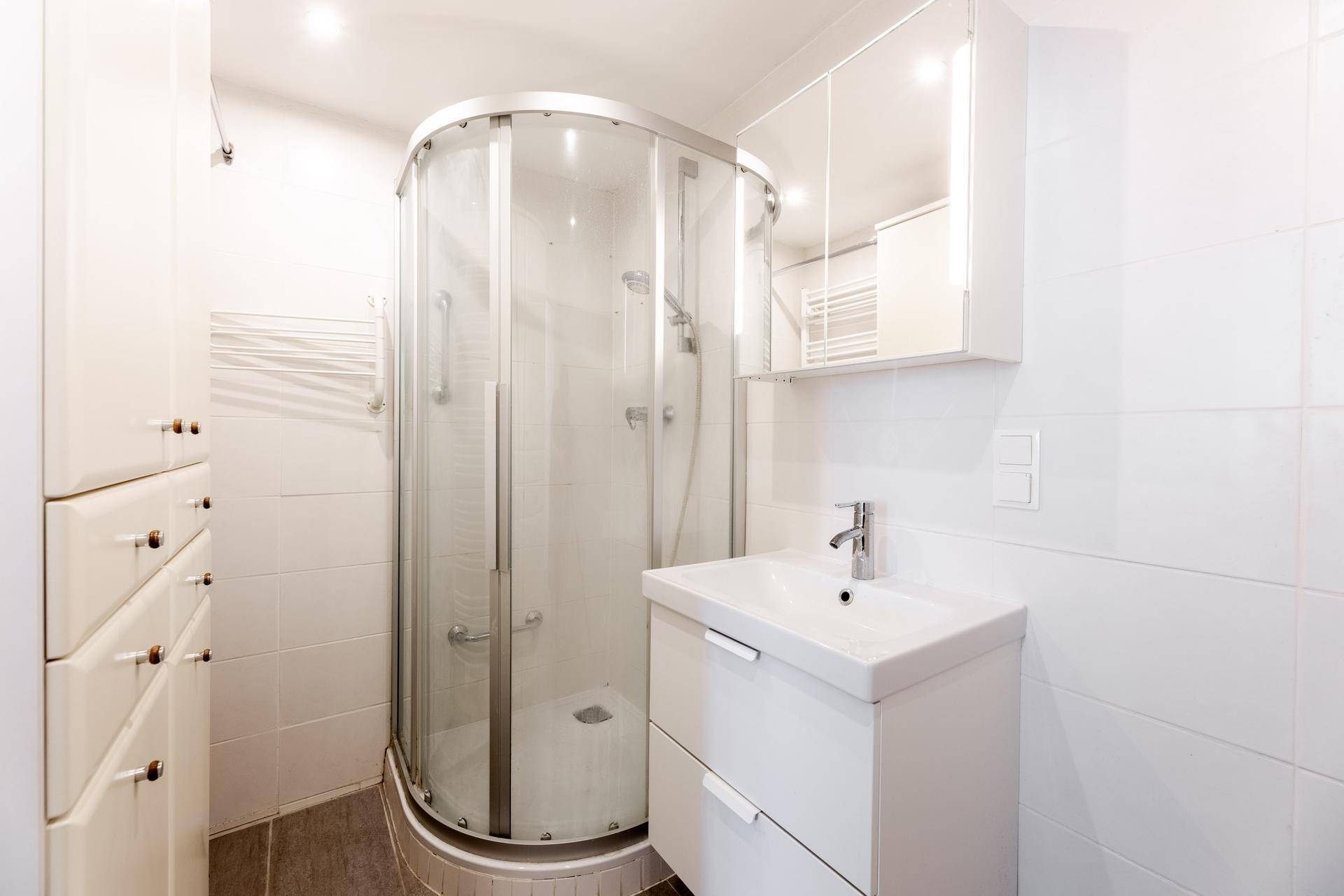 Modernes Badezimmer mit Duschkabine, Waschbecken und Spiegelschrank, komplett gefliest.