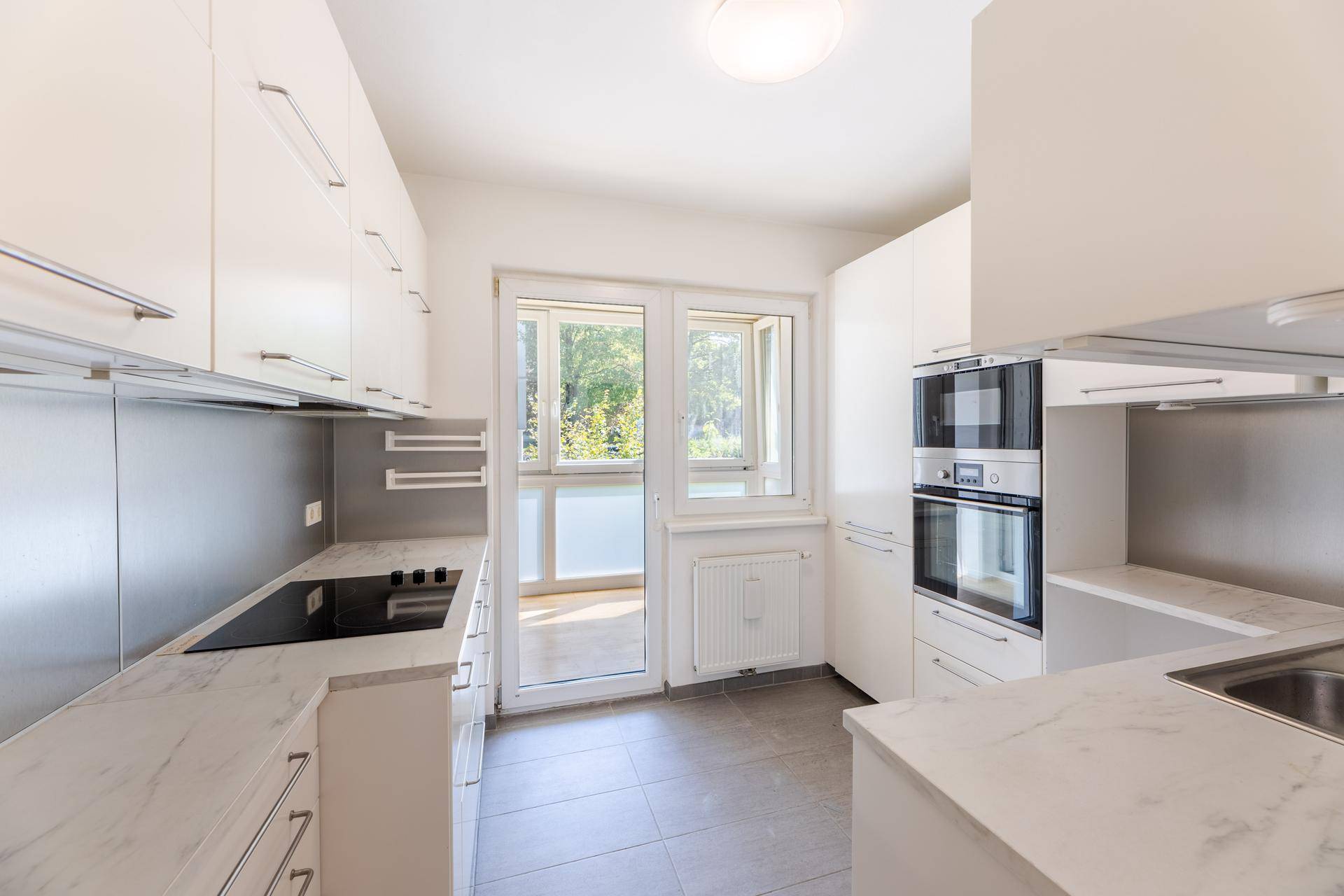 Helle Einbauküche mit weißen Fronten, modernen Geräten und Zugang zum Balkon.