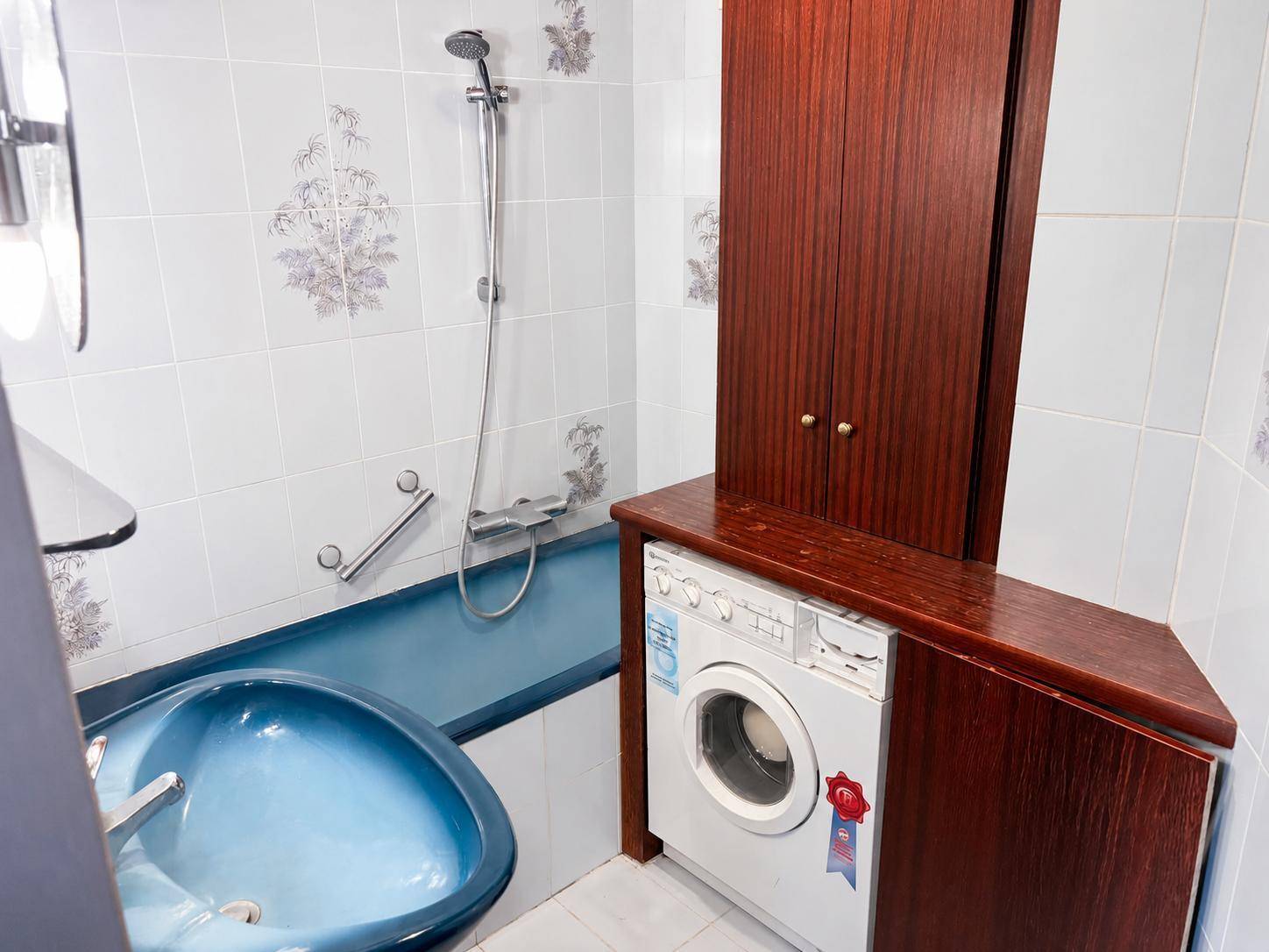 Badezimmer mit Badewanne, Dusche und Waschmaschine, ausgestattet mit blauen Akzenten.