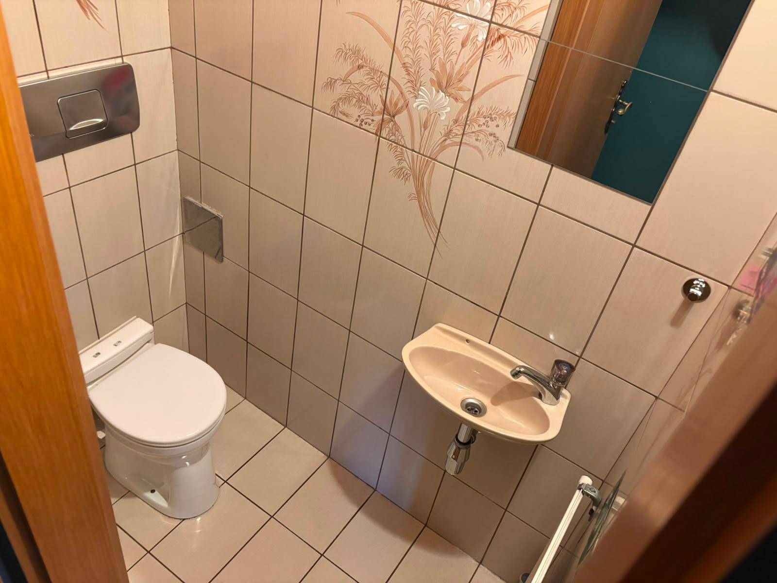 Kleines Gäste-WC mit beigen Fliesen, Wand-WC und einem kompakten Waschbecken.