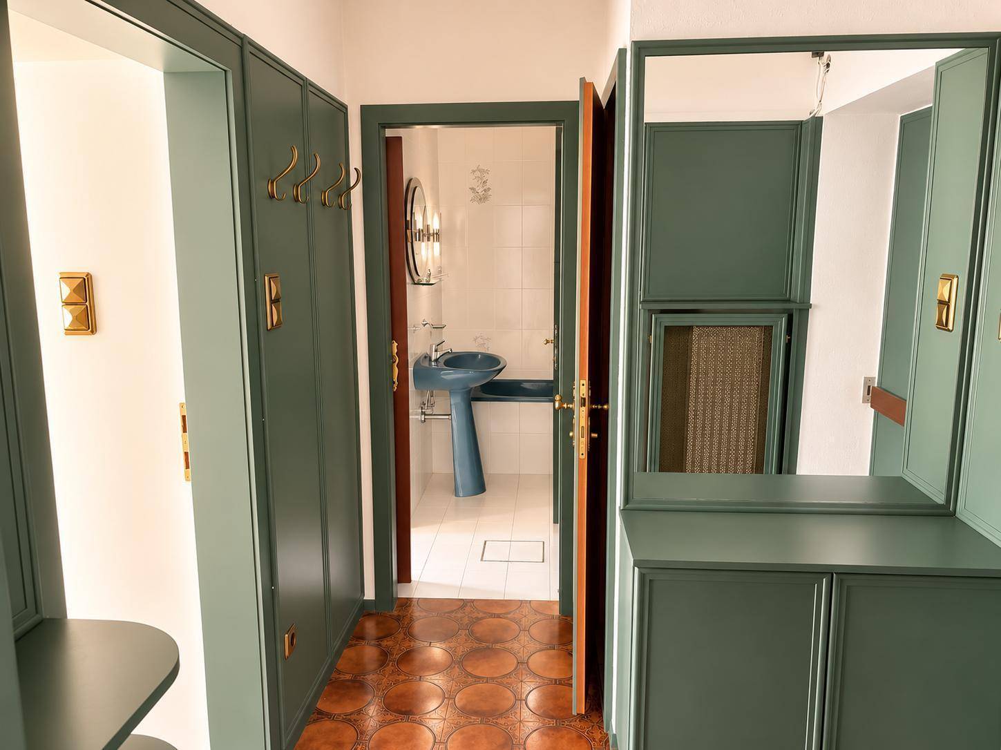 Flur mit grünen Einbauschränken und Blick in ein Badezimmer mit blauer Keramik.