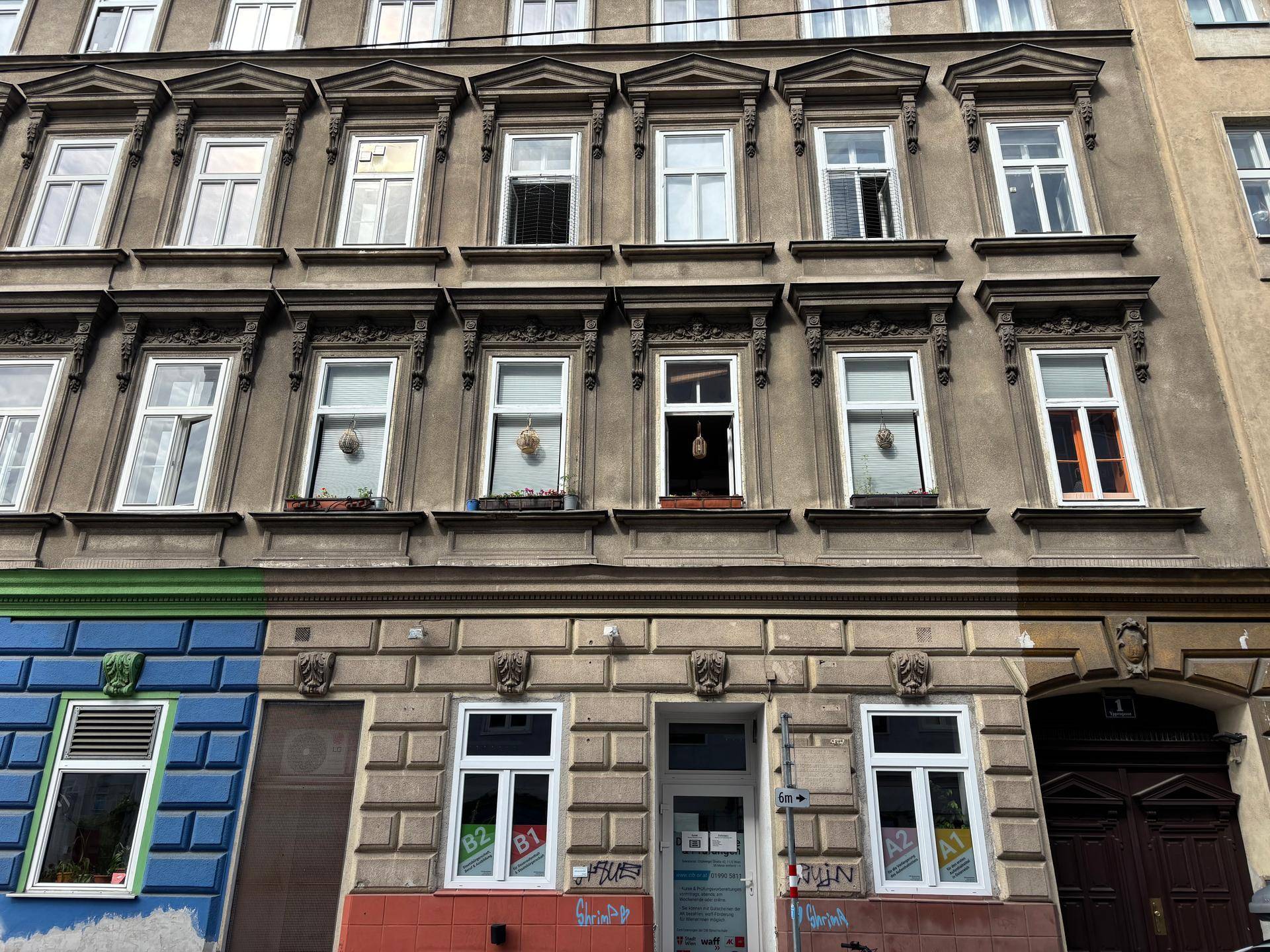 Historische Fassade eines Mehrfamilienhauses mit verzierten Fenstern und unterschiedlichen Erdgeschossgestaltungen.