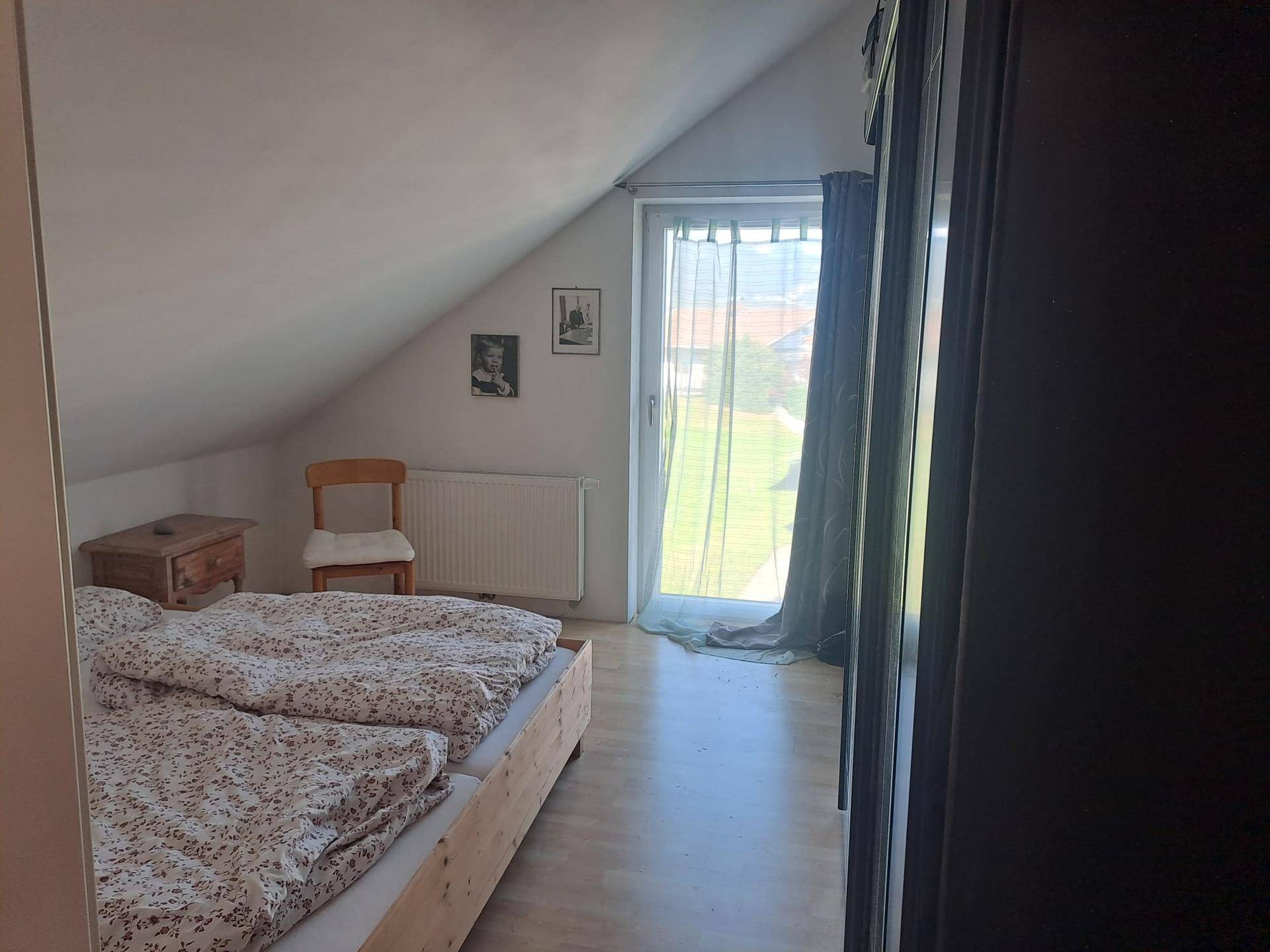 Schlafzimmer im Dachgeschoss mit schrägen Wänden, Holzboden und Zugang zum Außenbereich.