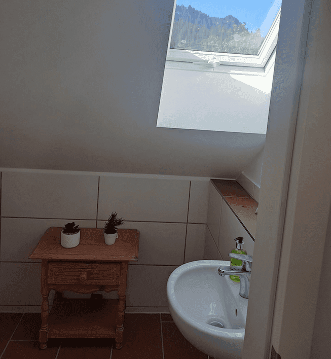 Kleines WC im Dachgeschoss mit Dachfenster, Waschbecken und Fliesenboden.
