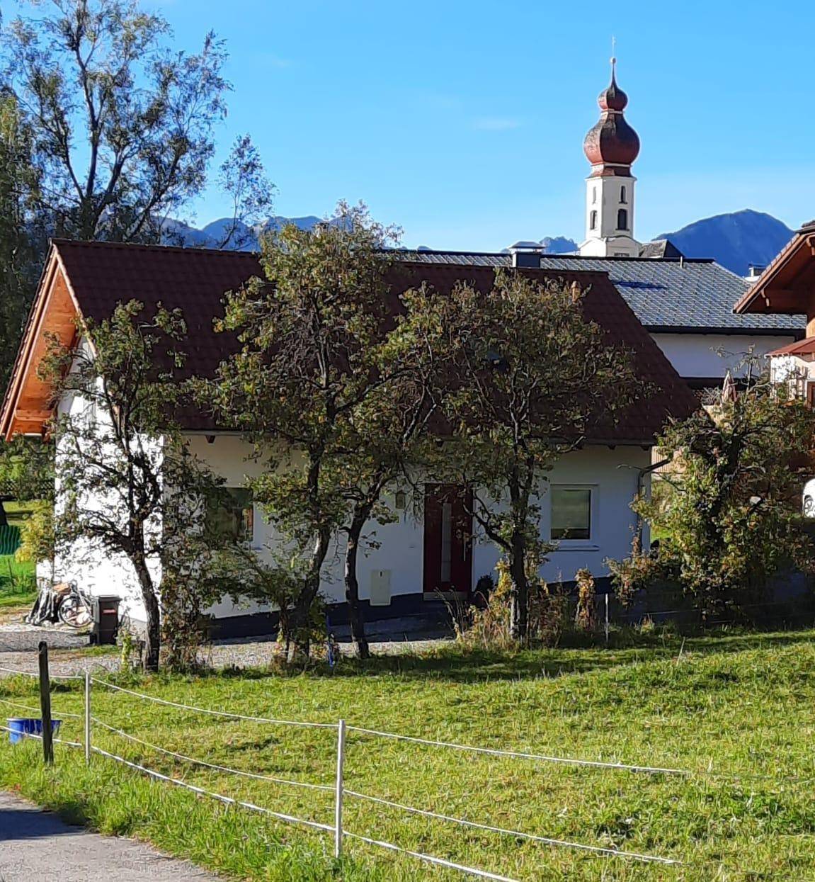 Vorderansicht des Einfamilienhauses mit Garten und einer Kirche im Hintergrund.