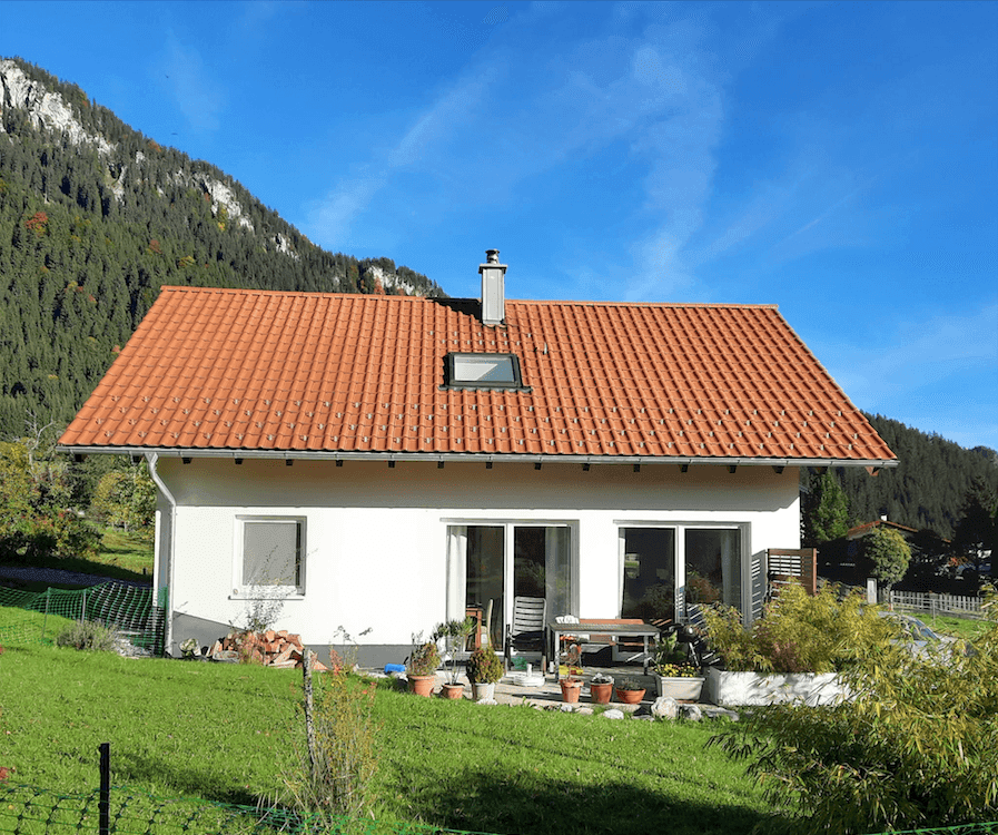 Rückseite des Hauses mit kleiner Terrasse, Gartenmöbeln und weitem Blick auf die Berge.