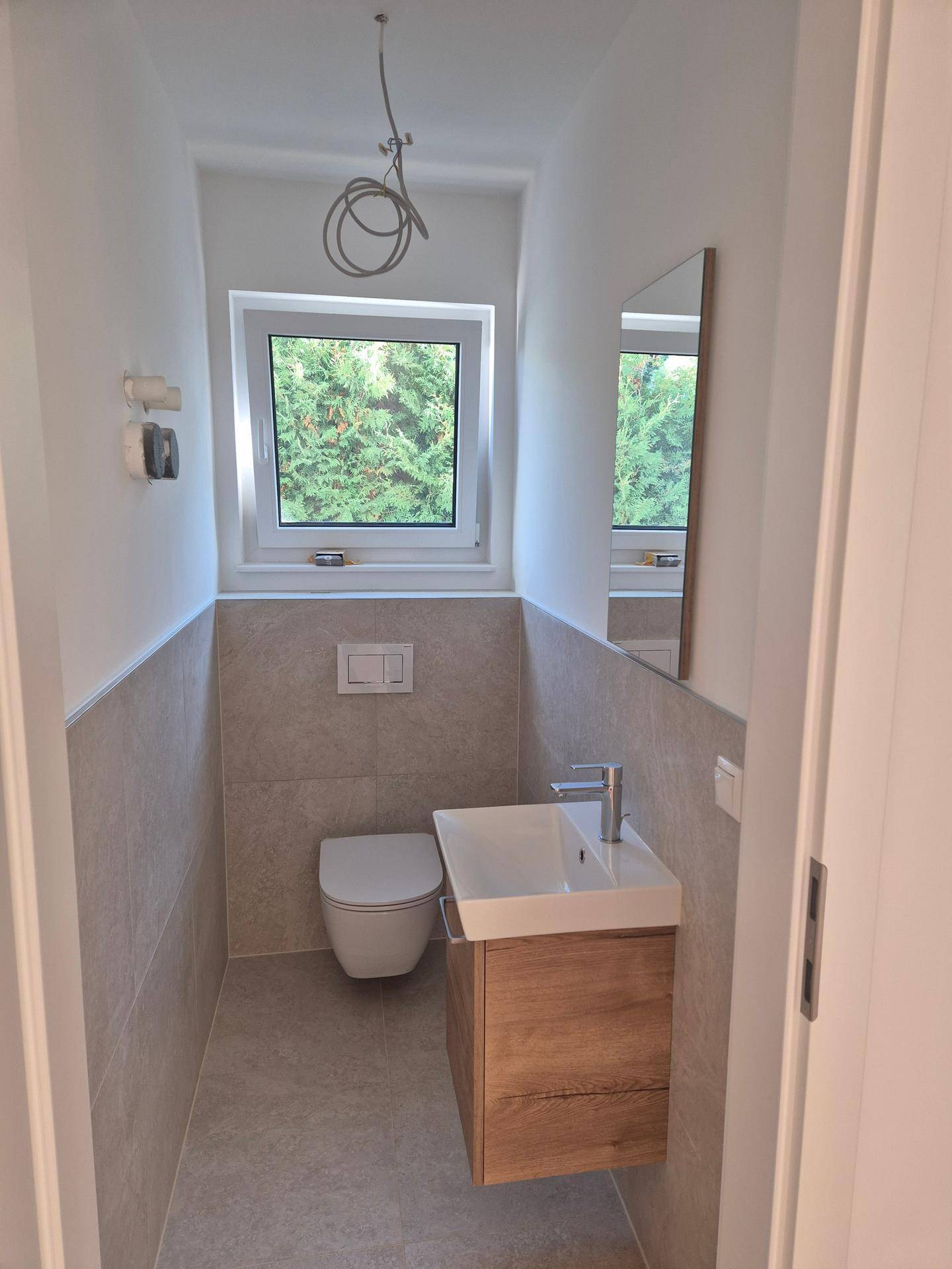 Kompaktes Gäste-WC mit wandhängender Toilette, kleinem Waschbecken und Fenster für Belüftung.