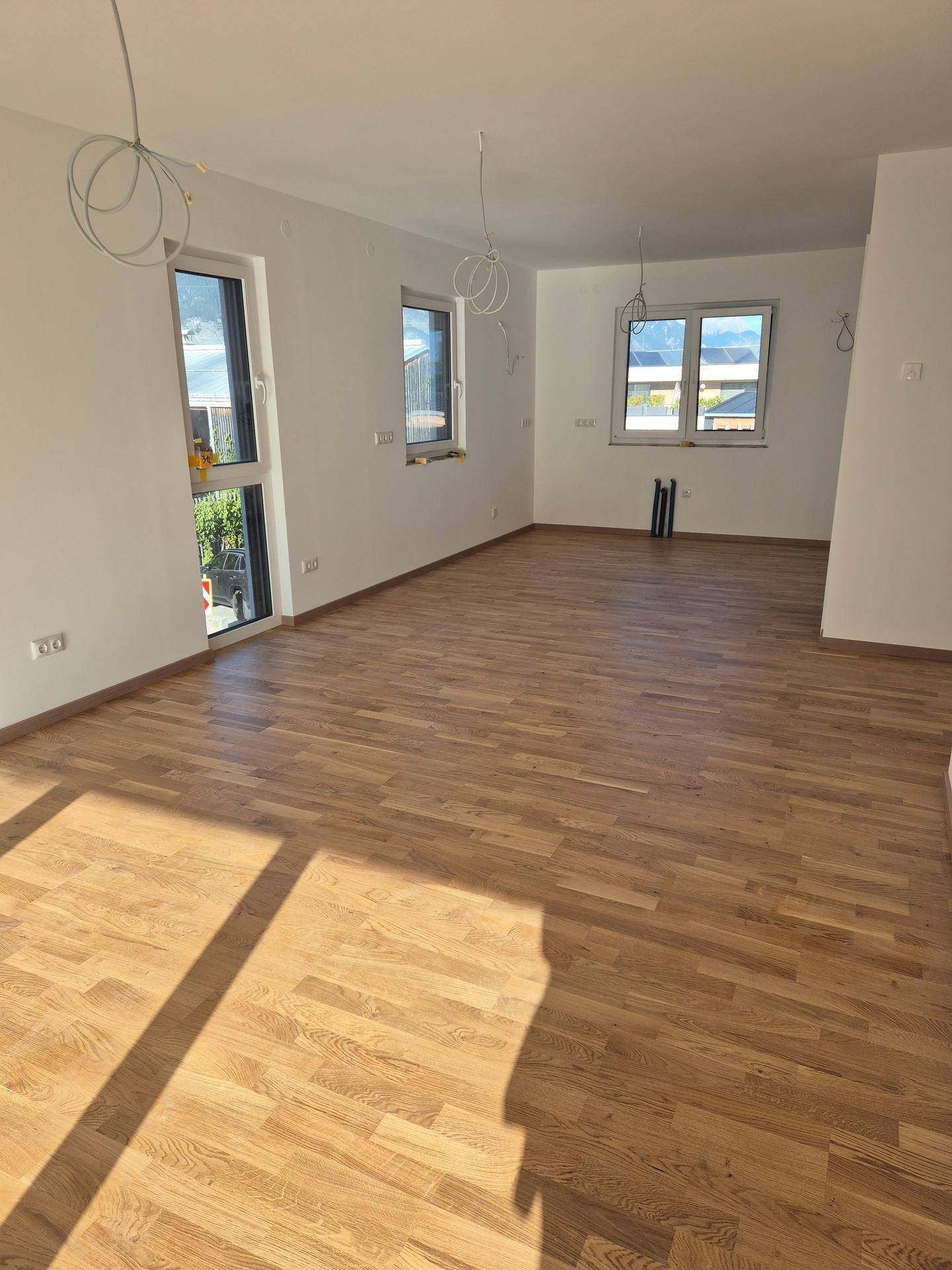 Geräumiges, unmöbliertes Zimmer mit hellem Holzboden und mehreren Fenstern, die viel Tageslicht hereinlassen.