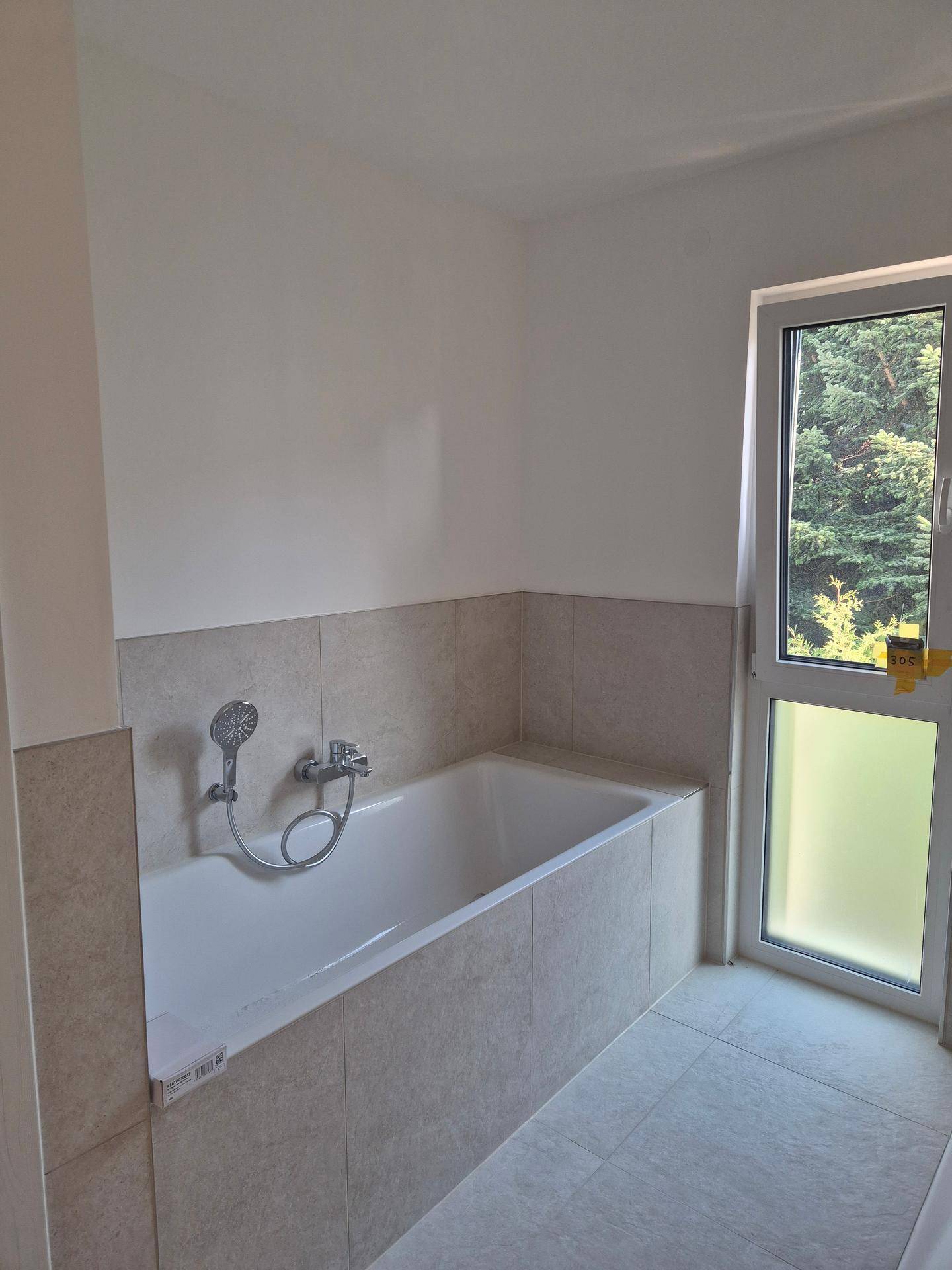 Modernes Badezimmer mit eingebauter Badewanne, hellen Fliesen und einem Fenster für Tageslicht.