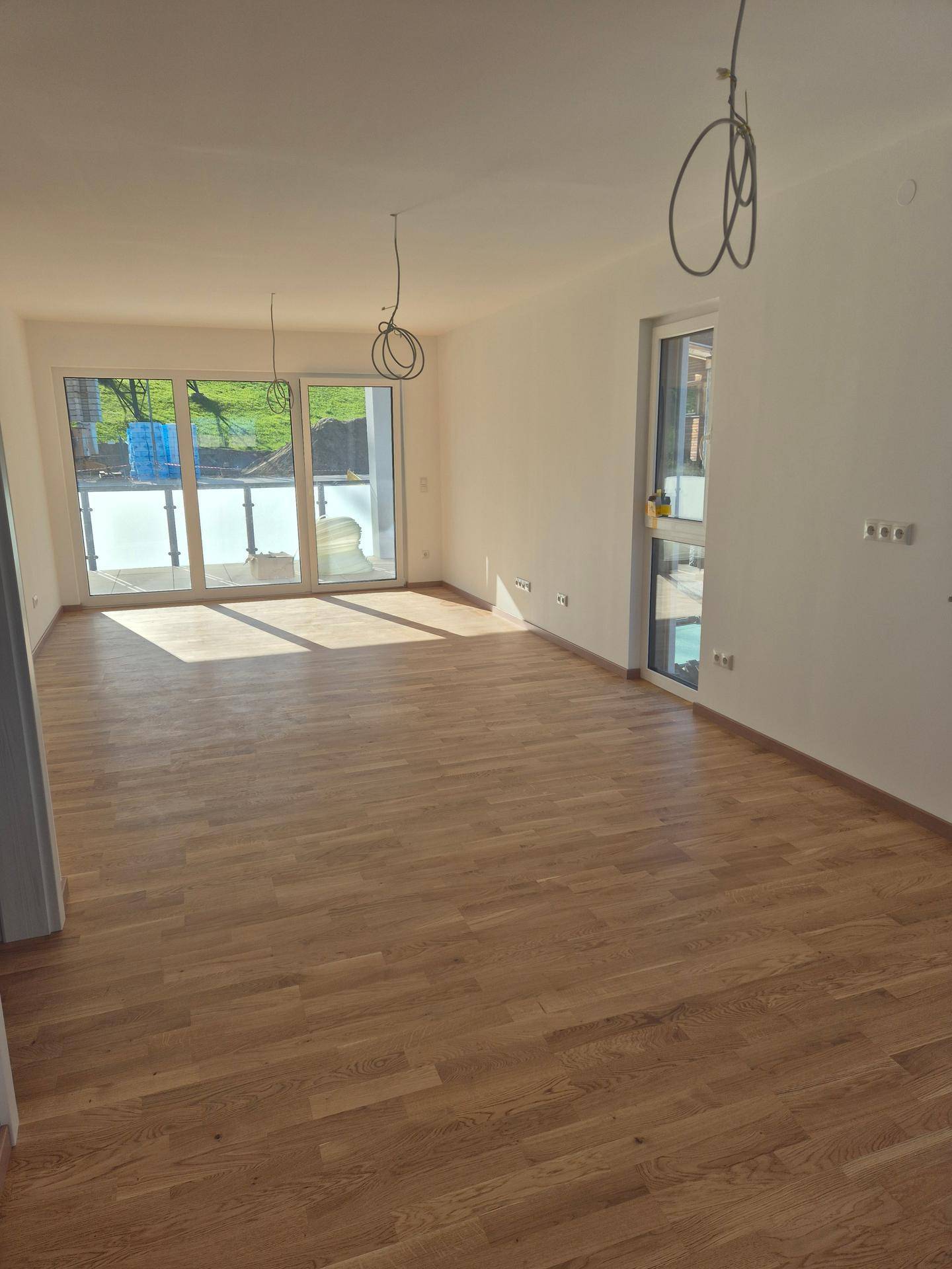 Helles, unmöbliertes Zimmer mit Holzboden und Zugang zu einem Balkon, ideal für einen Wohnbereich.