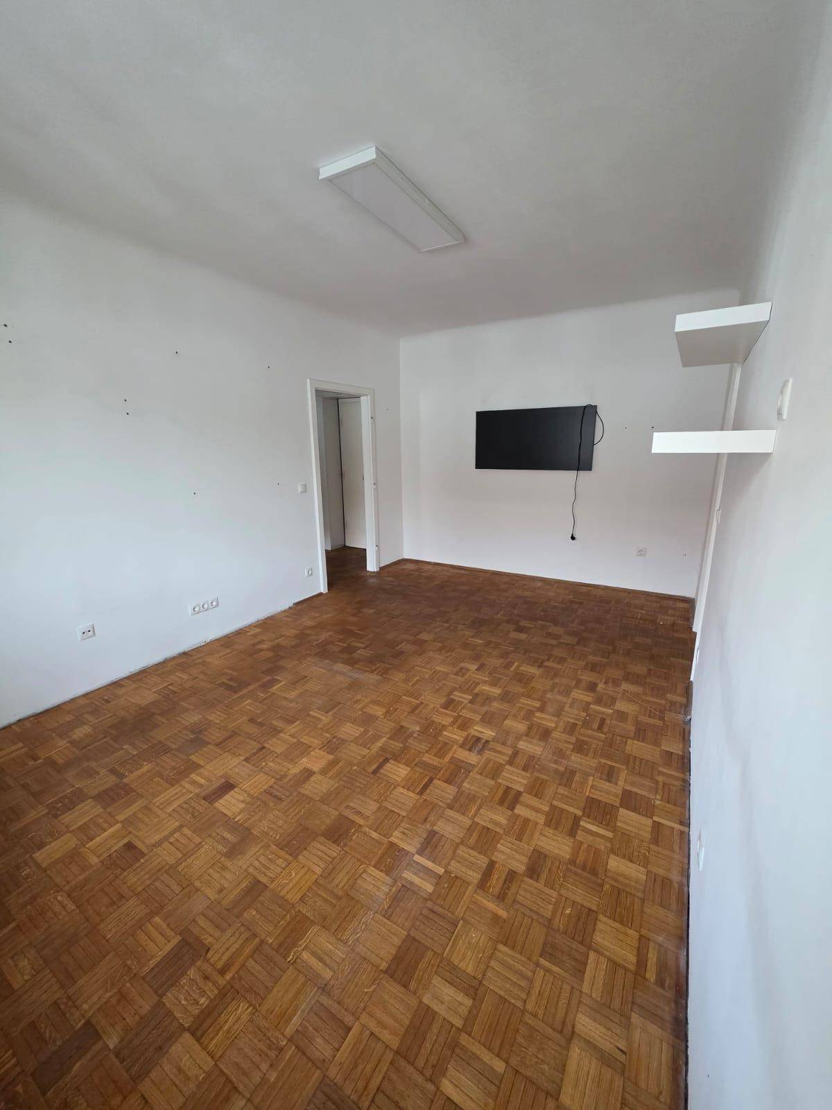 Großer, heller Raum mit Parkettboden und weiß gestrichenen Wänden.