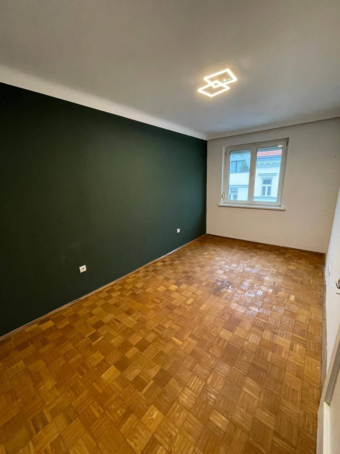 Helles Schlafzimmer mit einer dunkelgrünen Wand und klassischem Parkettboden.