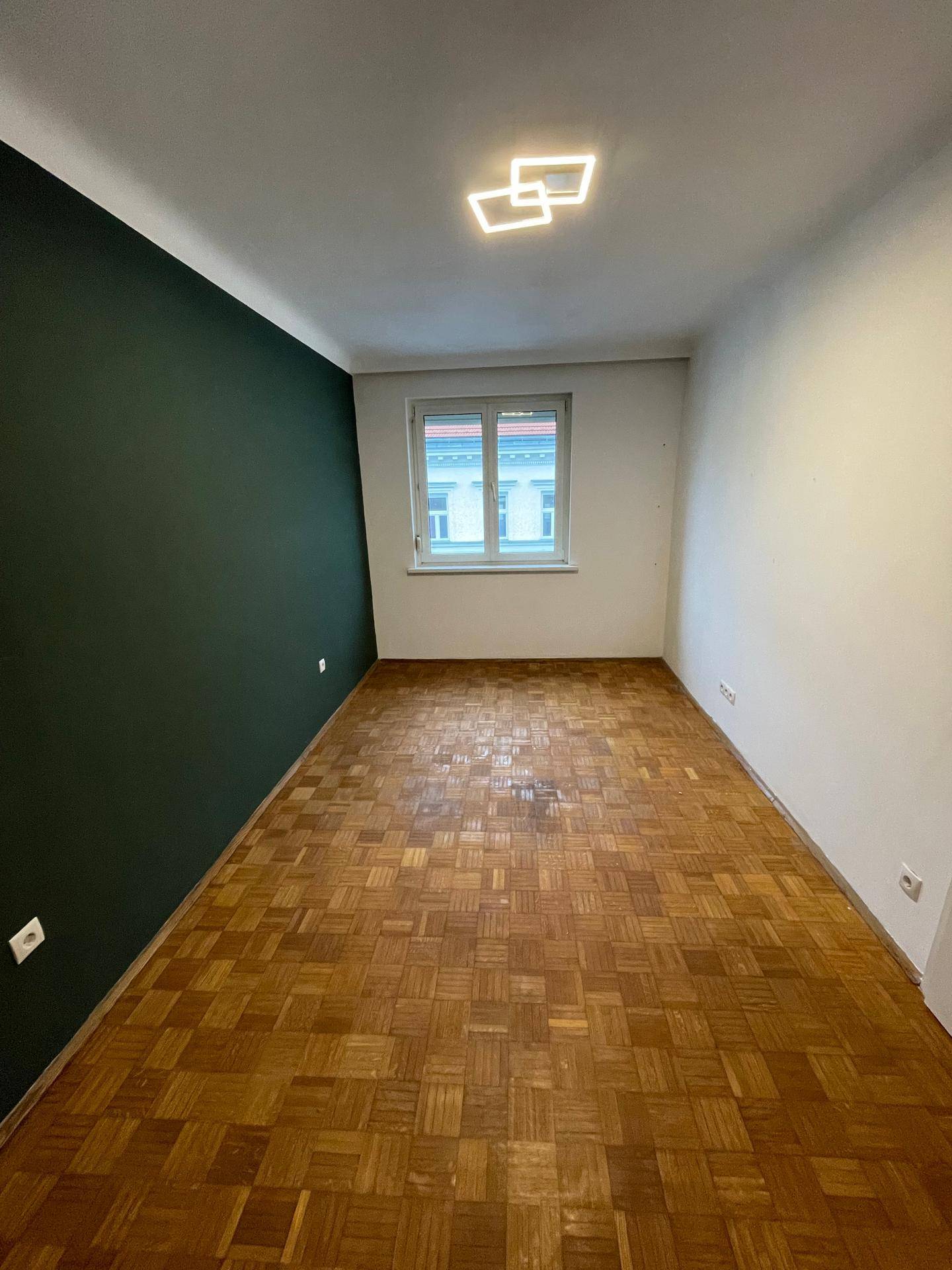 Schlafzimmer mit dunkler Akzentwand, Parkettboden und Fenster.