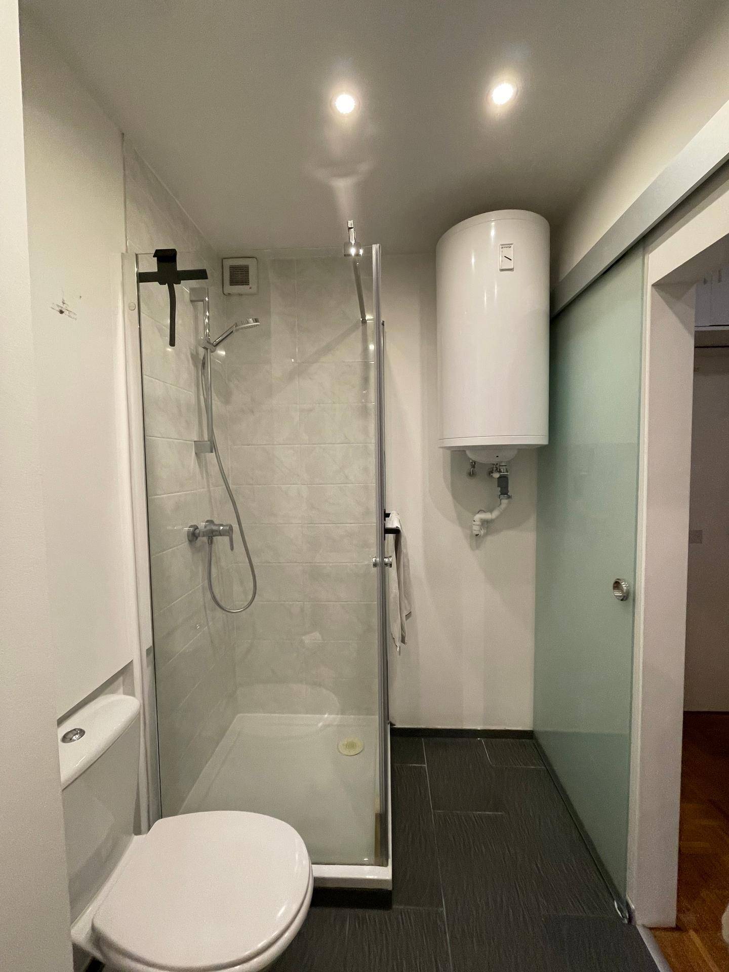 Kompaktes Badezimmer mit Duschkabine, Toilette und Warmwasserboiler.