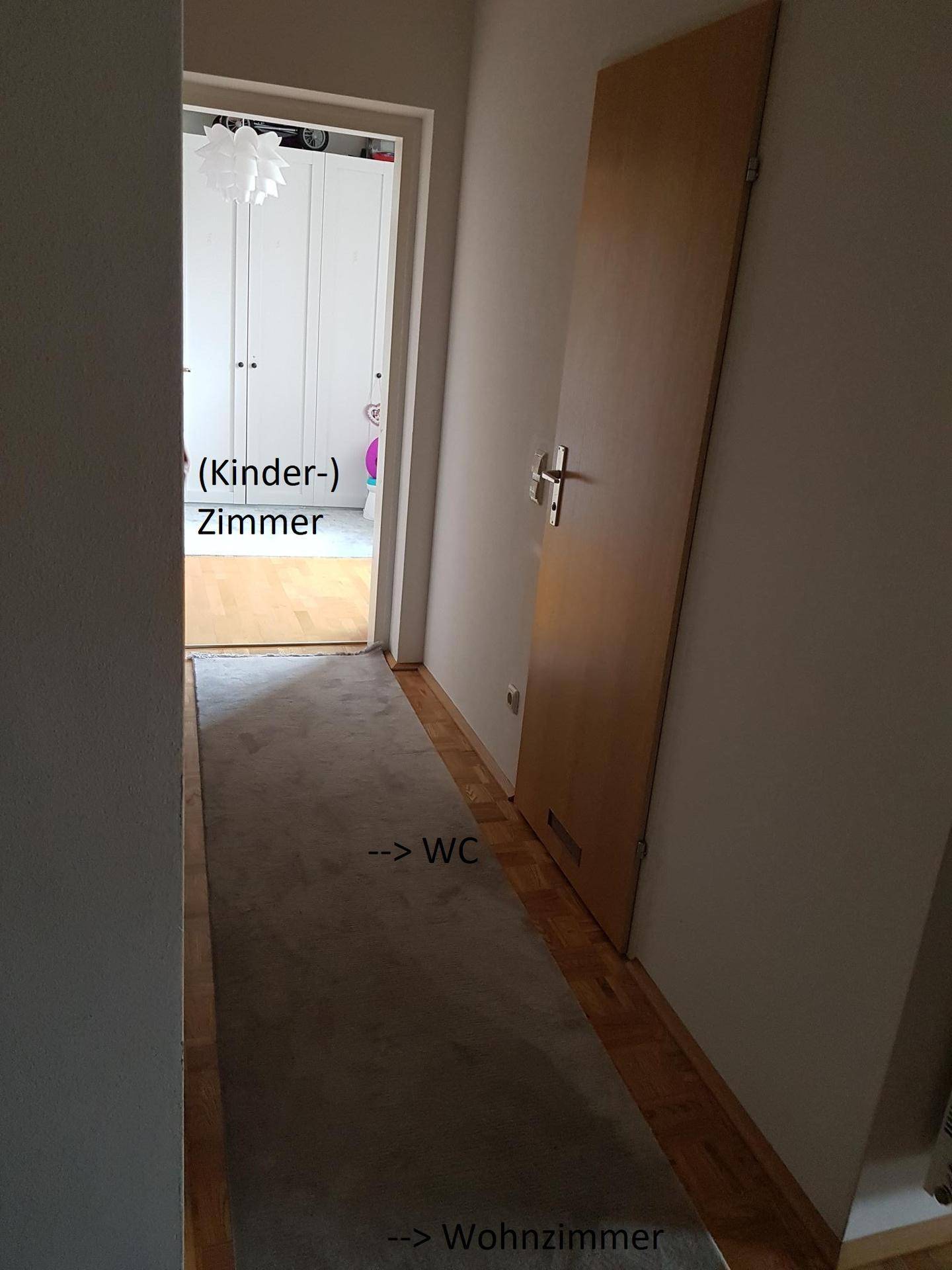 Langer Flur mit Teppichboden, der zu einem Kinderzimmer, WC und Wohnzimmer führt.