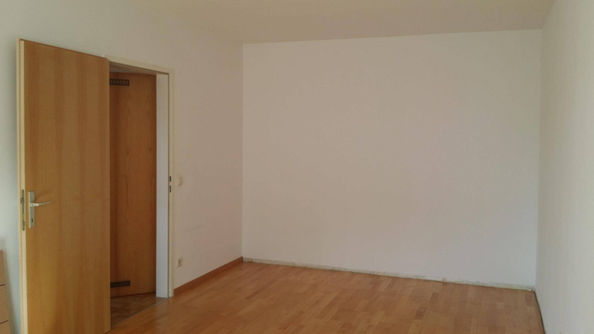 Leerer Raum mit hellem Parkettboden und einer Holztür, bereit zur individuellen Gestaltung.