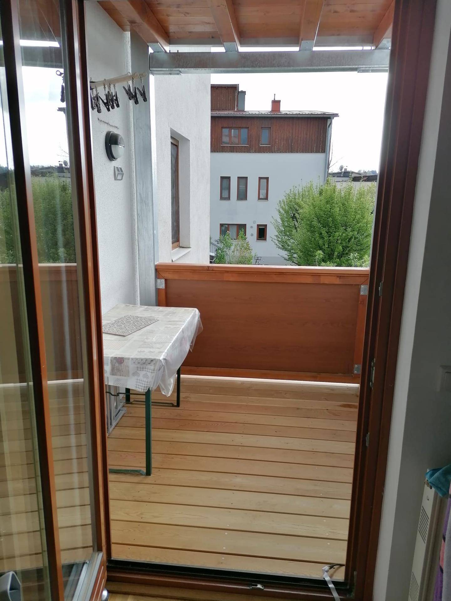 Gemütlicher Balkon mit Holzboden und einem kleinen Tisch, bietet Blick auf die umliegenden Gebäude.