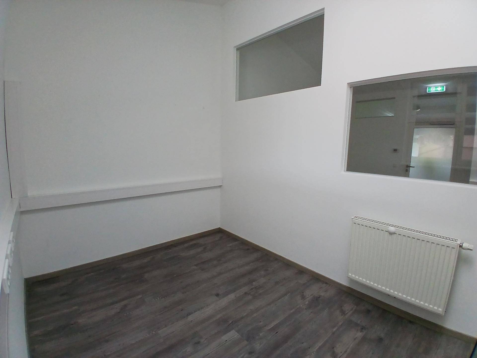 Ecke eines Büroraums mit Laminatboden, Heizkörper und kleinen Fenstern für zusätzliche Belichtung.