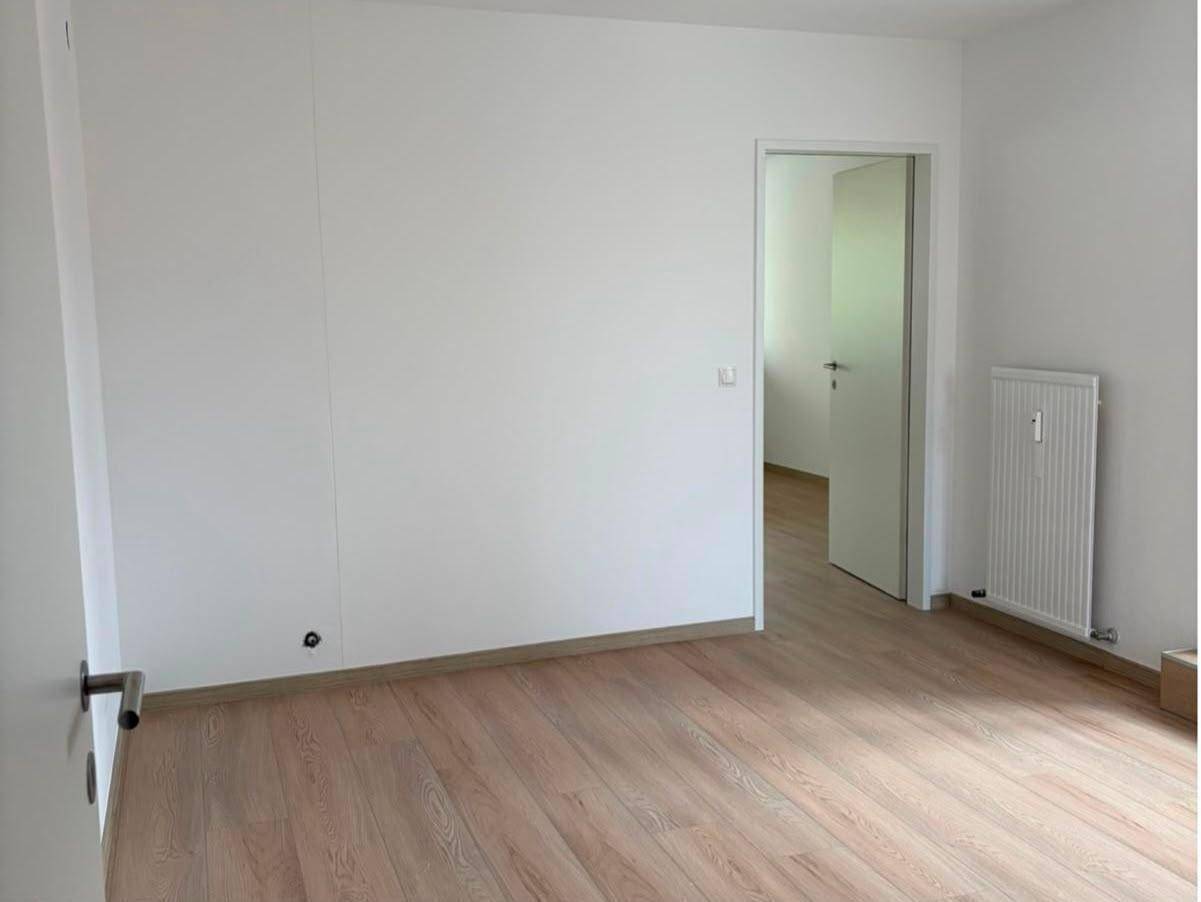 Geräumiger, heller Raum mit weiß gestrichenen Wänden und hellem Holzfußboden, bereit zum Einzug.