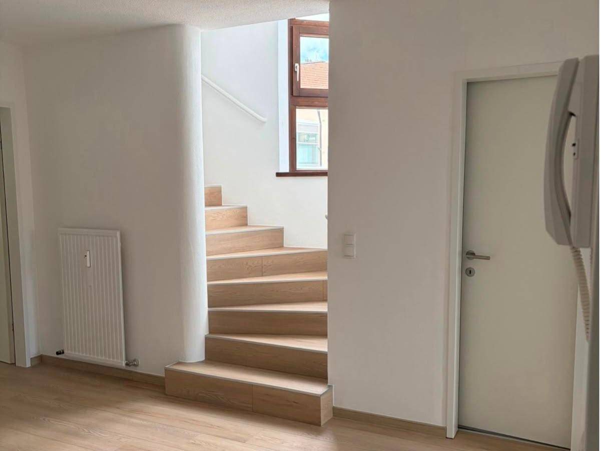 Heller Treppenaufgang mit Holzstufen und einem Fenster, das für natürliches Licht sorgt.