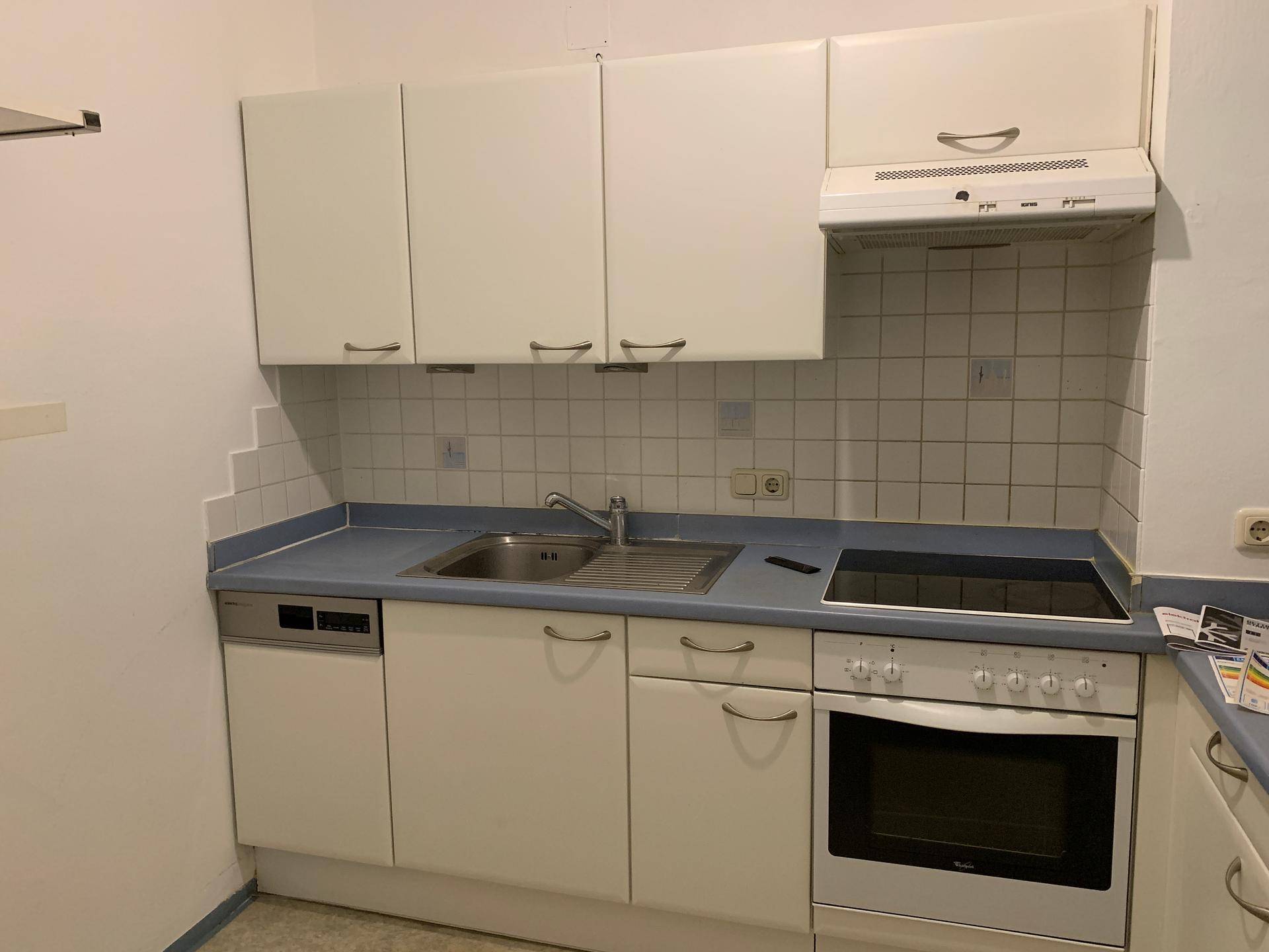 Funktionale Küche mit weißen Schränken, blauer Arbeitsplatte, Spülmaschine und Kochfeld.