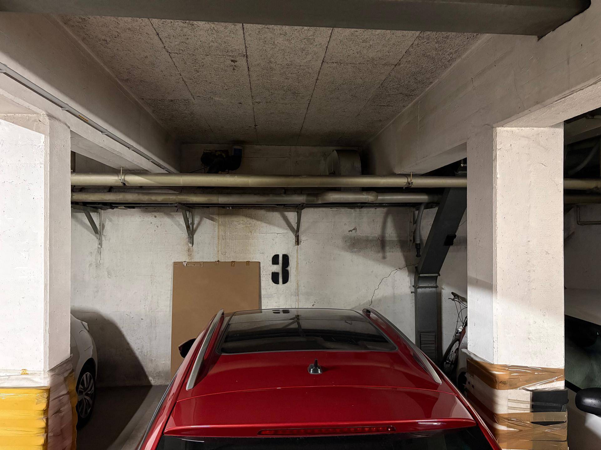 Tiefgarage mit Betonstruktur und einem geparkten roten Auto, bietet sicheren Stellplatz.
